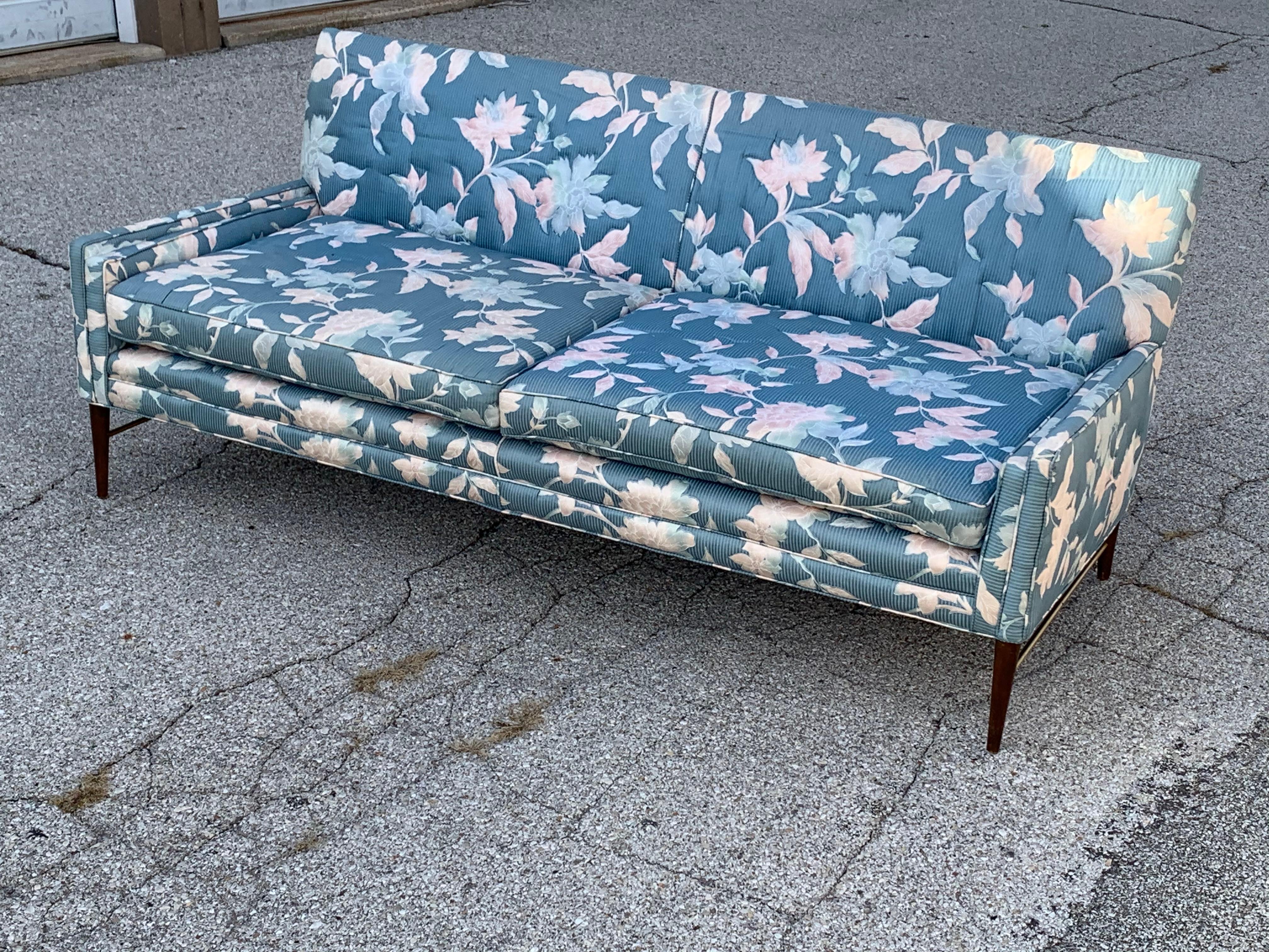 1950s Mid-Century Modern Paul McCobb for Directional sofa on tapered legs with round brass  stretcher from front to back and side to side. Drop arm detail, older floral upholstery needs updating, foam is good. Original finish on legs, warm patina to