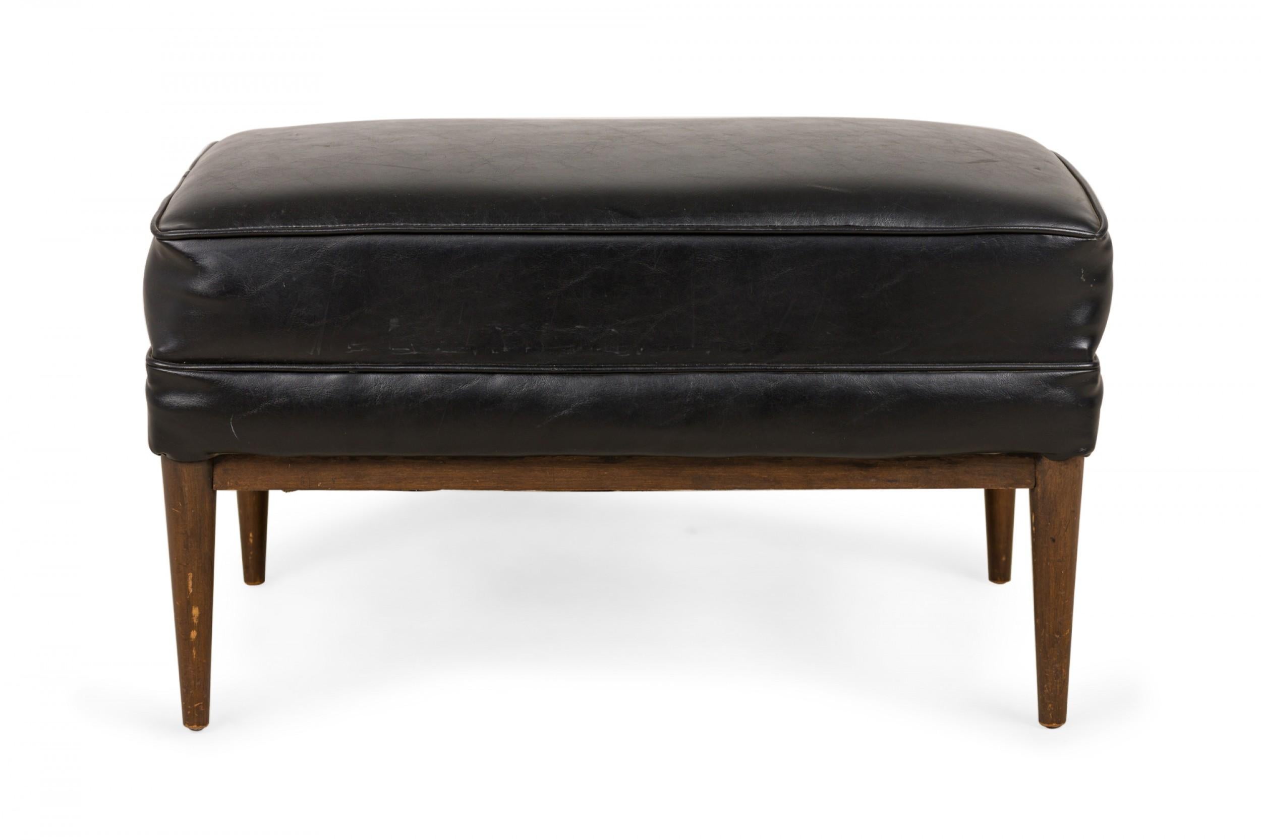 American mid-century rectangular ottoman with a black vinyl upholstered top resting on a walnut base with tapered legs. (PAUL MCCOBB FOR DIRECTIONAL)