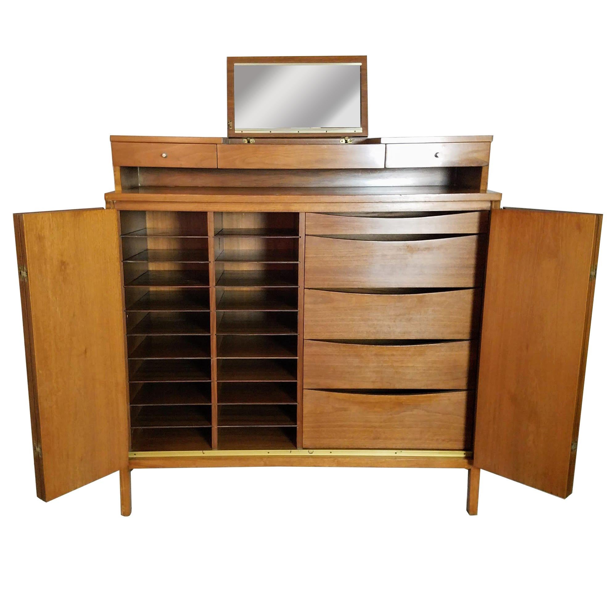 Paul McCobb's gentleman's walnut chest with a fold down mirror Irwin line for Calvin.
The accordion doors are bookmatched veneer opening to 18 shirt shelves and five graduated drawers.
The chest is in very good vintage condition with wear