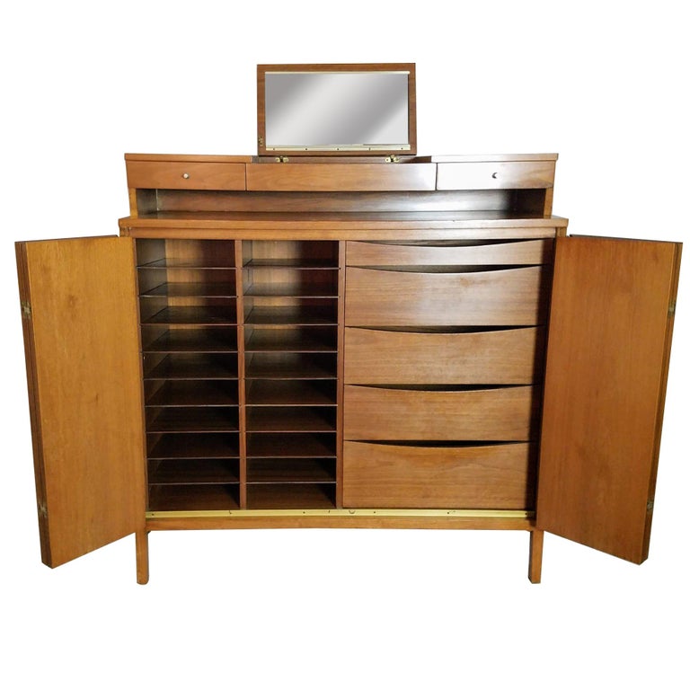 Paul McCobb's gentleman's walnut chest with a fold down mirror Irwin line for Calvin.
The accordion doors are bookmatched veneer opening to 18 shirt shelves and five graduated drawers.
The chest is in very good vintage condition with wear