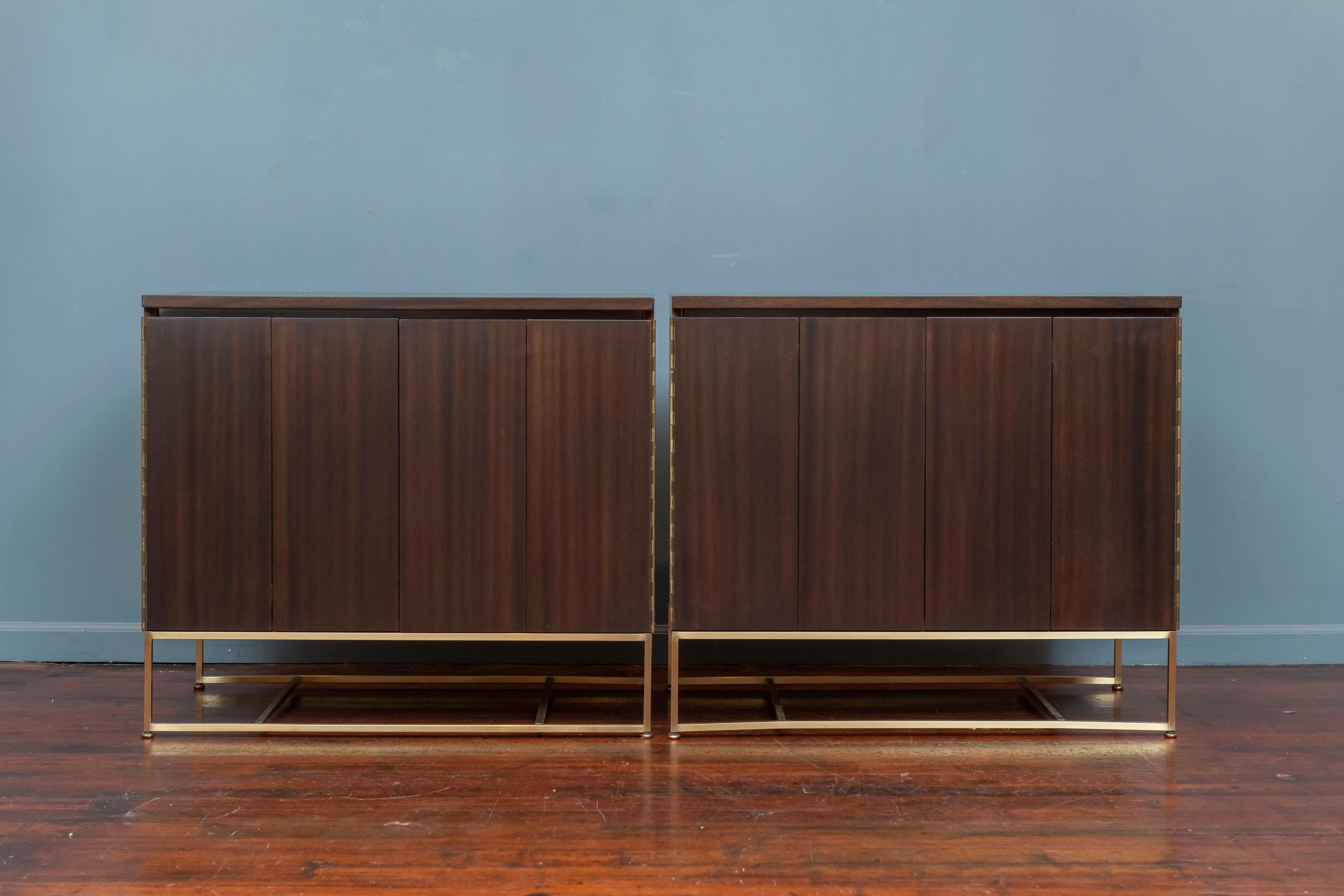 Paul McCobb design pair of cabinets for his Irwin Collection for Calvin Group. 
An original matched pair of mahogany and brass bi-fold door cabinets each with a single drawer and one adjustable shelf. Newly refinished cases in a dark brown semi