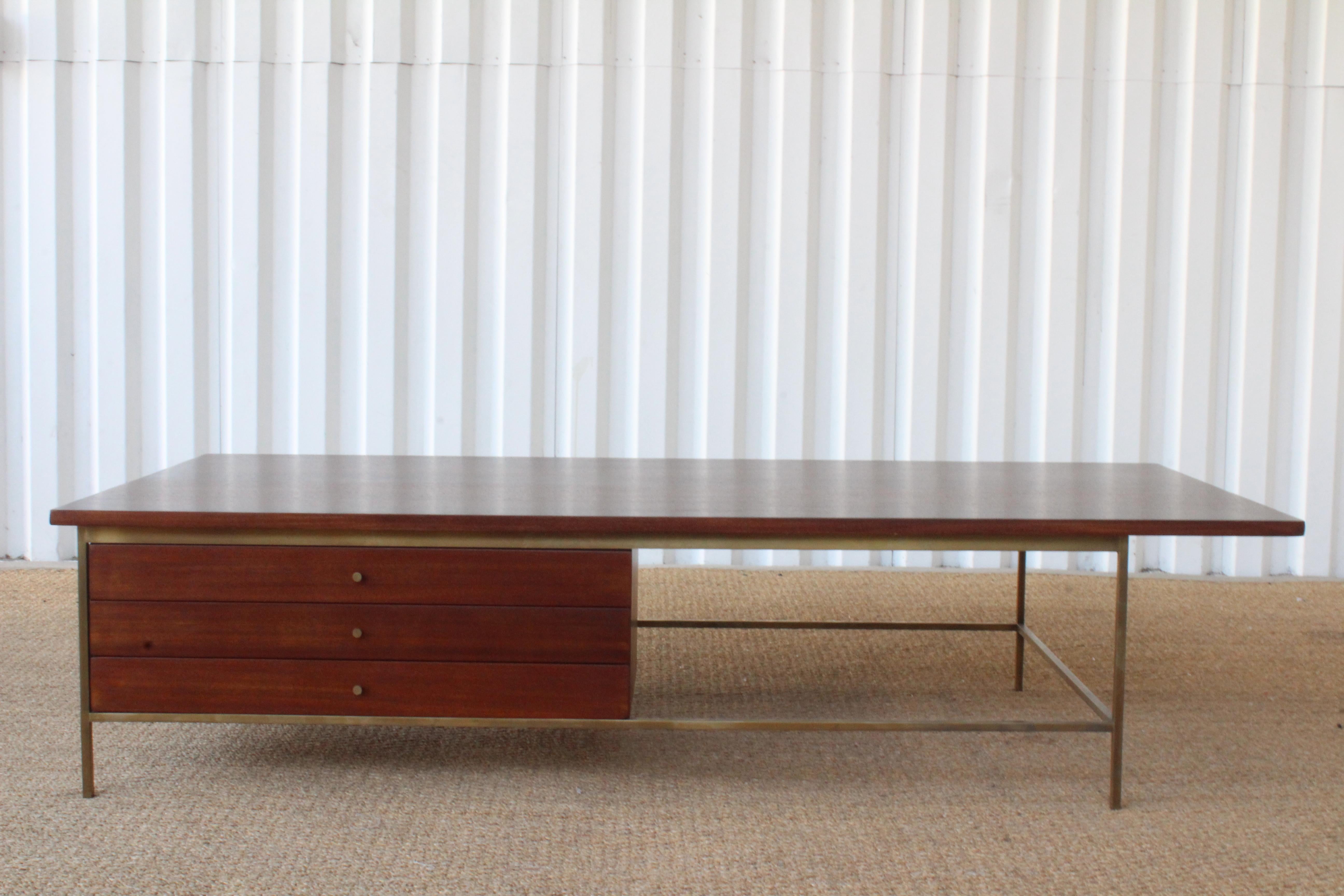 Vintage 1950s coffee table designed by Paul McCobb, part of the Irwin Collection for Calvin Furniture. Features a brass base and mahogany top with three drawers. The mahogany has been recently refinished. There are a few minor veneer repairs.