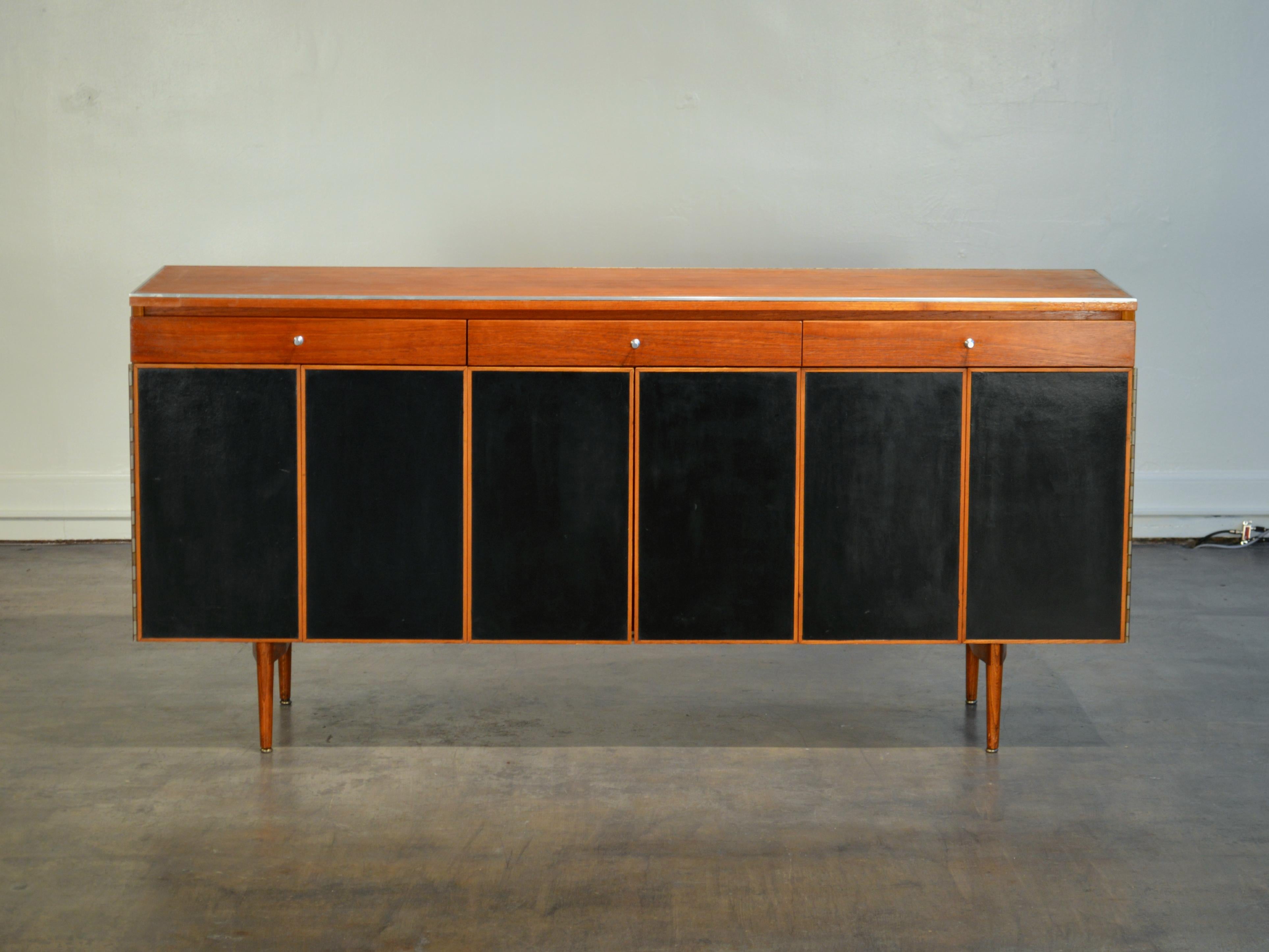 Finished sideboard with accordion doors designed by Paul McCobb as part of the Irwin collection. Made by Calvin Furniture of Gran Rapids Michigan, circa 1957. Credenza features mahogany and black leather finishes throughout: Leather cabinet fronts,