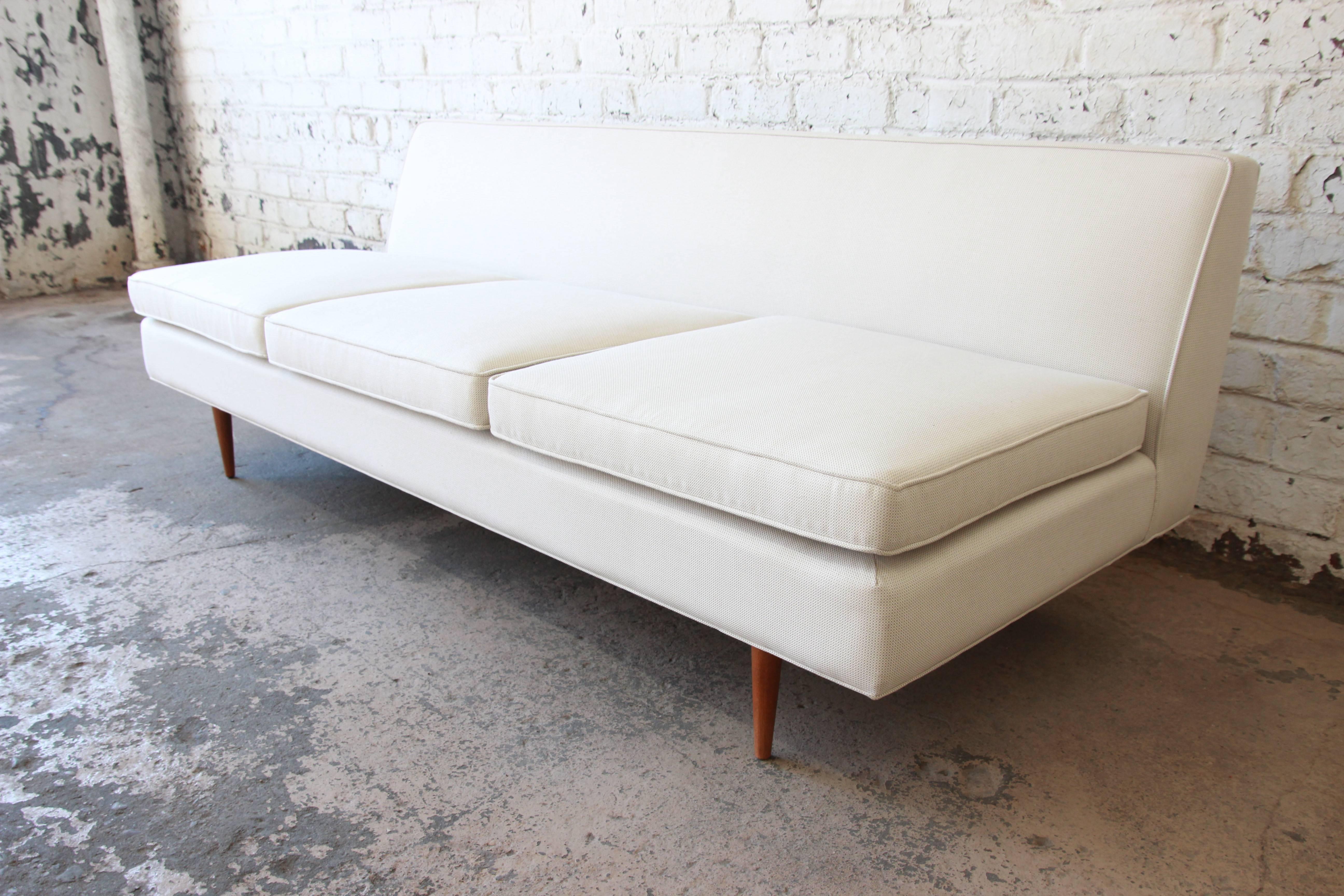 Offering an exceptional Mid-Century Modern armless sofa designed by Paul McCobb. The sofa features sleek mid-century design and thin tapered solid walnut legs. It has been professionally restored with new springs, foam, and crosshatch Knoll