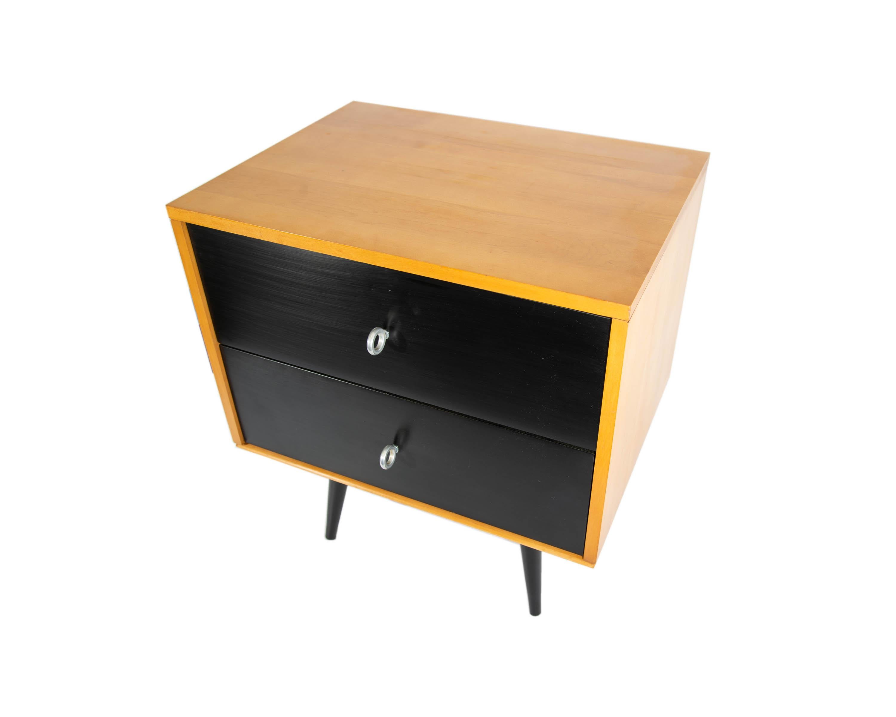 A pair of Planner Group maple night stands designed by American designer Paul McCobb (1917-1969). Each iconic stand has two black lacquered drawers with round steel pulls. Each night stand chest rests on a platform base. The base is raised on four