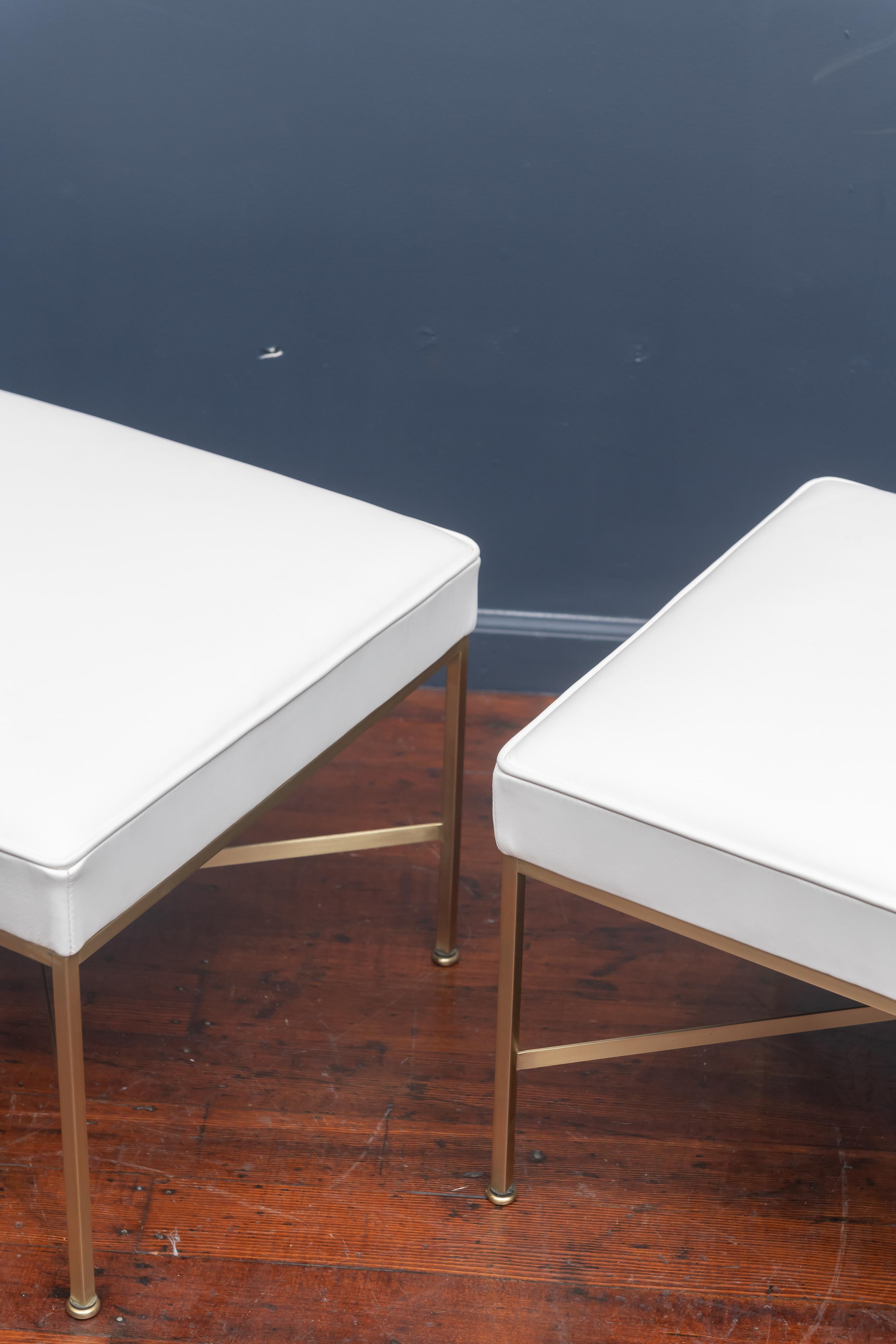 Pair of Paul McCobb X-base brass ottomans newly upholstered in off white leather.