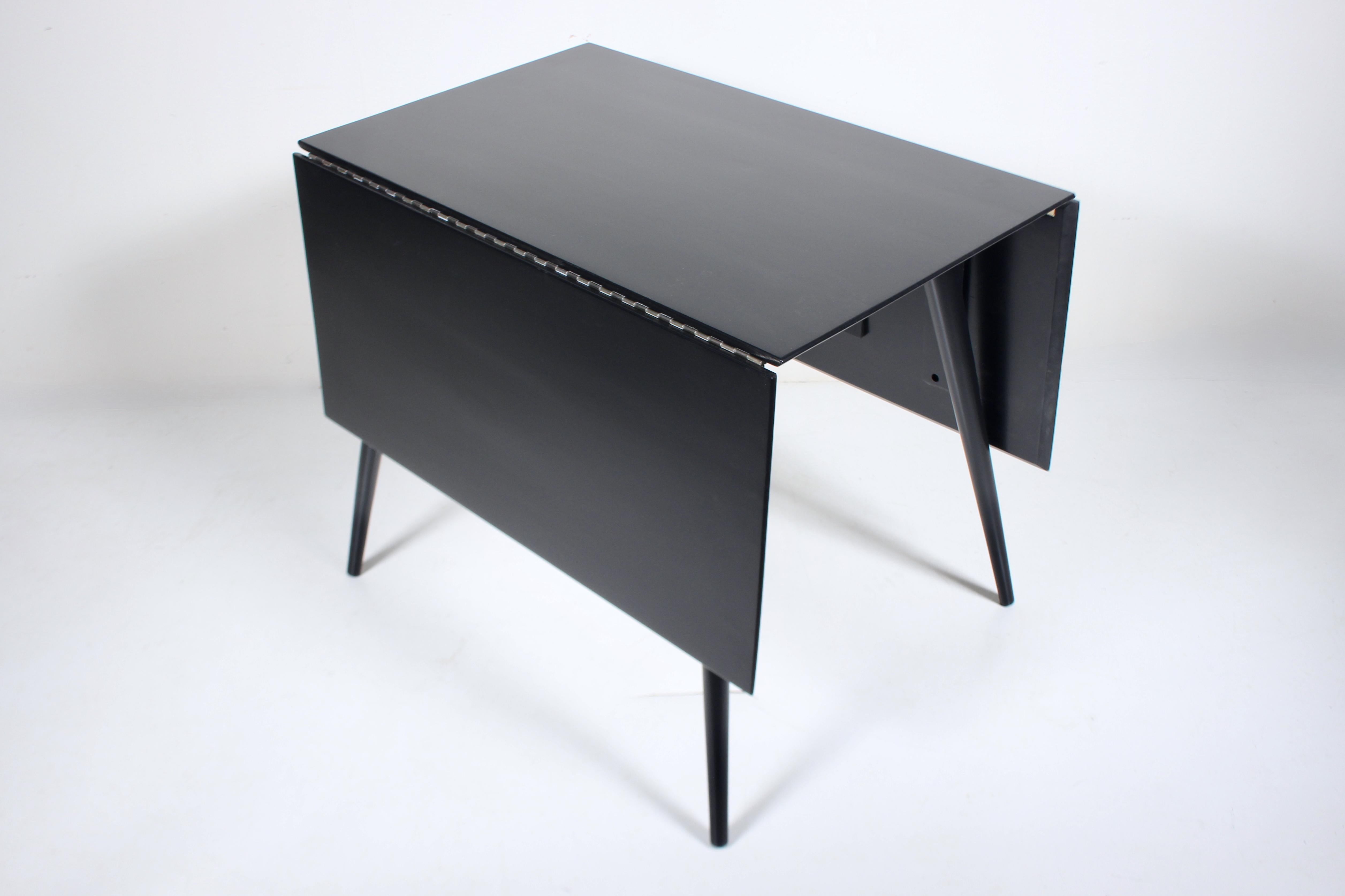 Table à abattant noire de Paul McCobb #1524, de style moderne américain du milieu du siècle.  Forme rectangulaire en bois massif émaillé noir, avec charnière piano, reposant sur des pieds fuselés arrondis. Table ouverte 56 