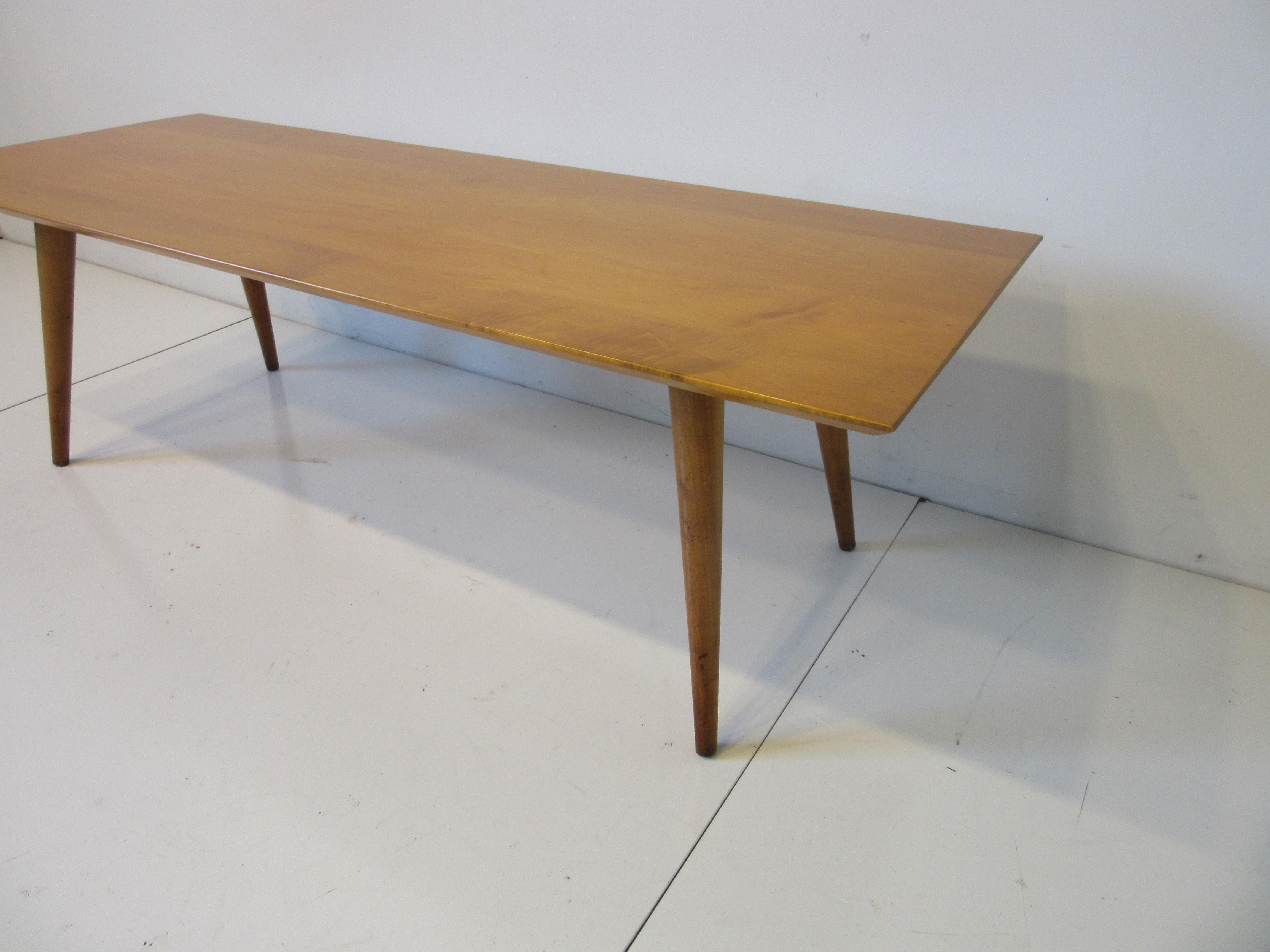 A solid maple wood coffee table with tapered edges sitting on conical legs, a simple well crafted piece by one of the mid century's most iconic designers Paul McCobb. For the Winchendon Furniture Company from their Planner Group Collection.