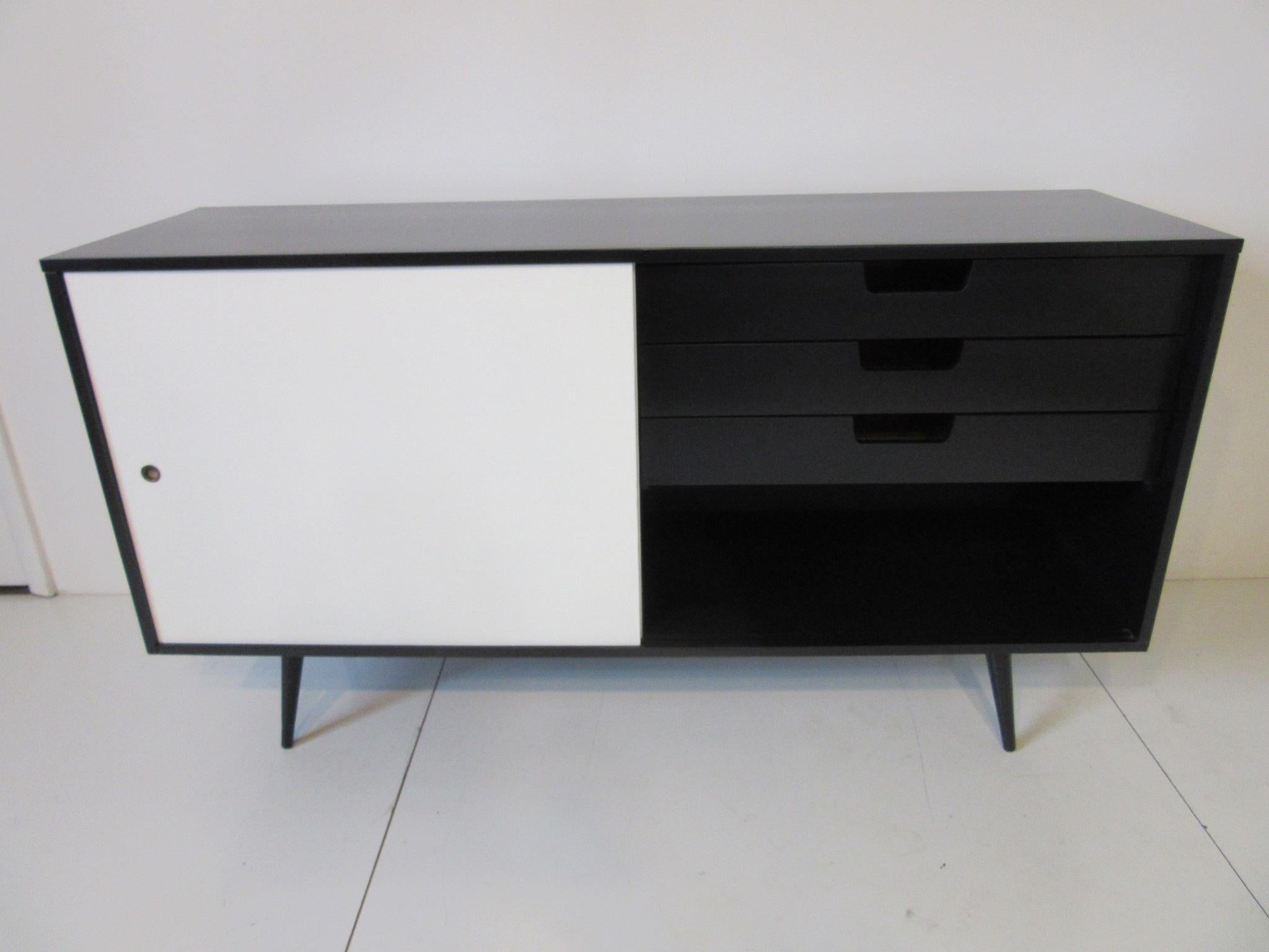A satin black solid wood credenza with three drawers to the right side and one drawer with an adjustable shelve plus storage to the left side. Two siding white doors give this piece a tailored and thigh look, manufactured by the Winchendon furniture