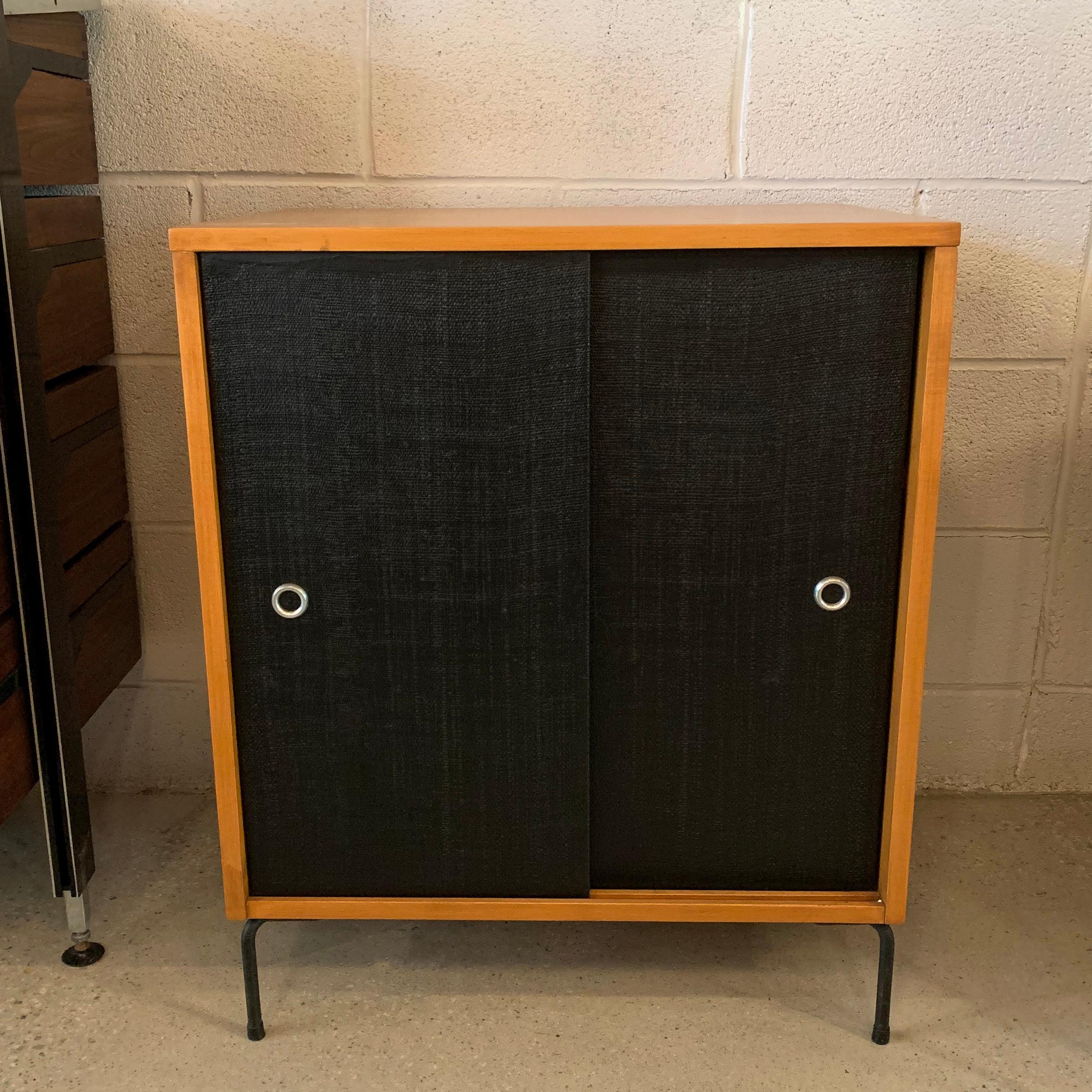 Mid-Century Modern cabinet by Paul McCobb, Planner Group, Winchendon features a solid natural maple body with contrasting black grass cloth sliding door fronts and added wrought iron legs.