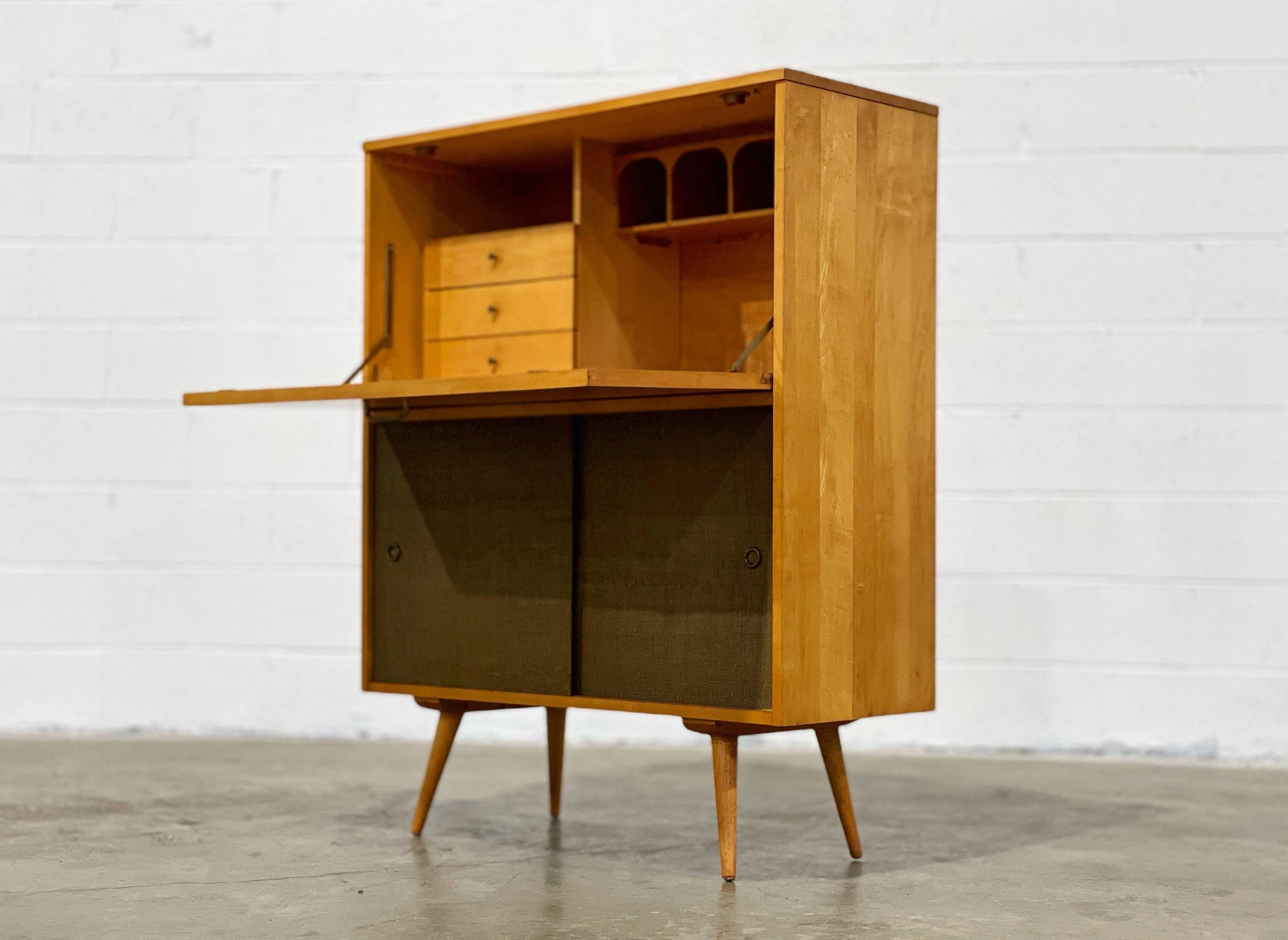Stellar Paul McCobb model 1564-b drop down desk with moss green grasscloth sliding doors, circa 1953. This example is unique on the market currently. Desirable inset splayed tapered legs. Adjustable lower shelf behind the grasscloth doors. Three
