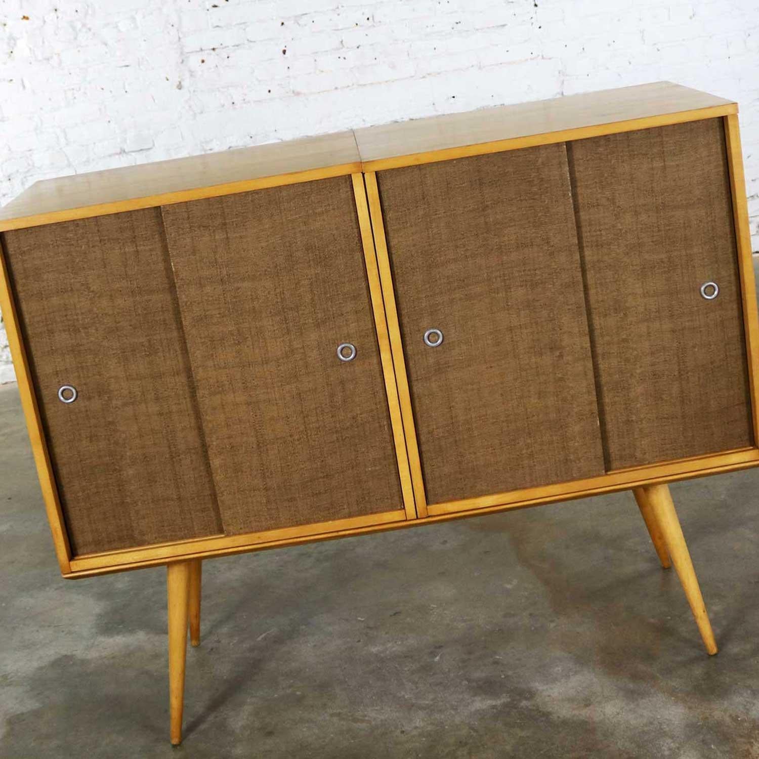 Iconic pair of Mid-Century Modern vintage sliding door cabinets with grasscloth covering on the solid natural maple bench platform base from the Planner Group designed by Paul McCobb for Winchendon makes up this three-piece set. All three pieces are