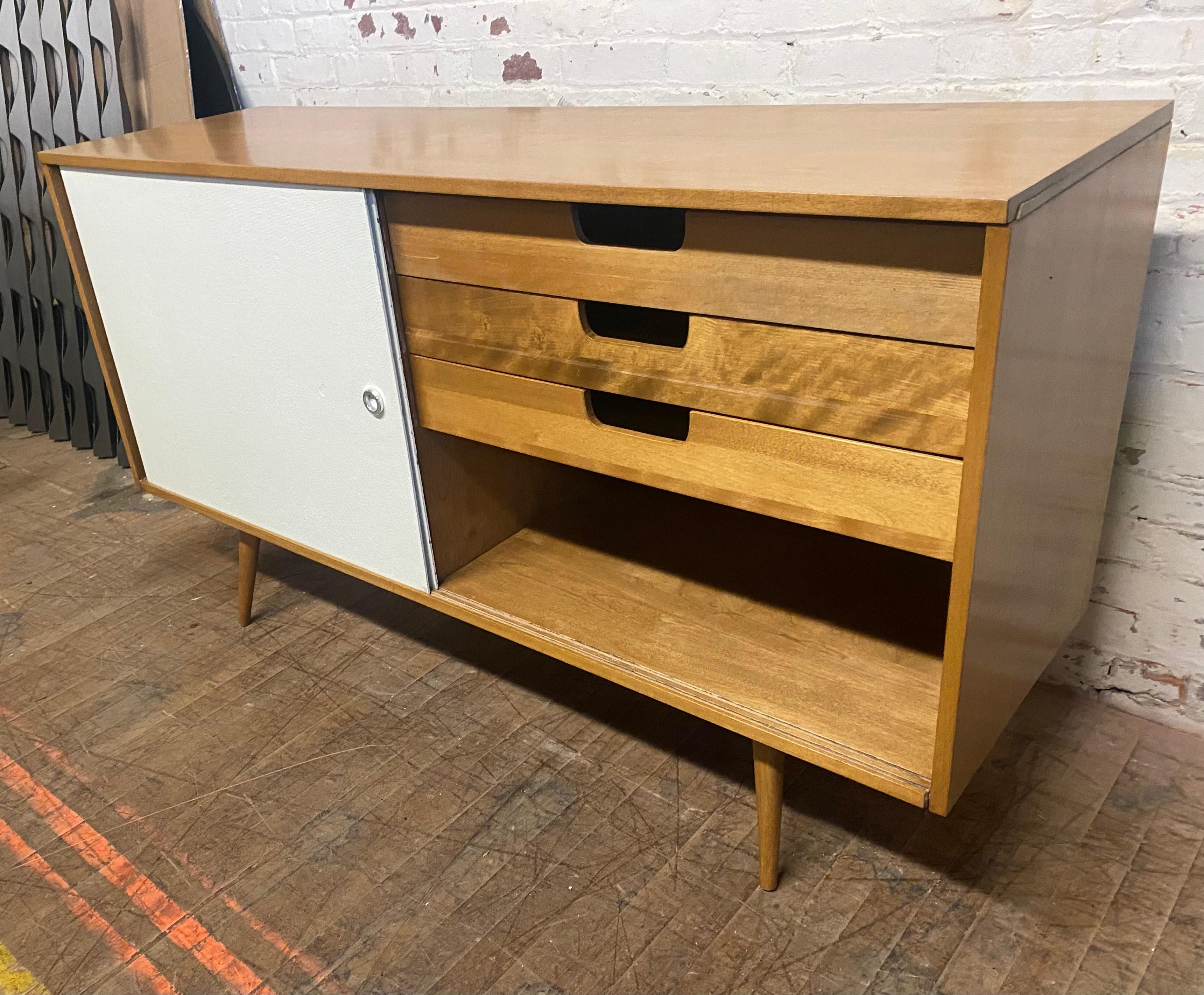 From the Paul McCobb Modular Planner Group line of Winchendon Furniture. Solid maple cabinet holds three drawers on one side single drawer with adjustable shelf on opposing side. All hidden behind sliding doors covered in original painted grass