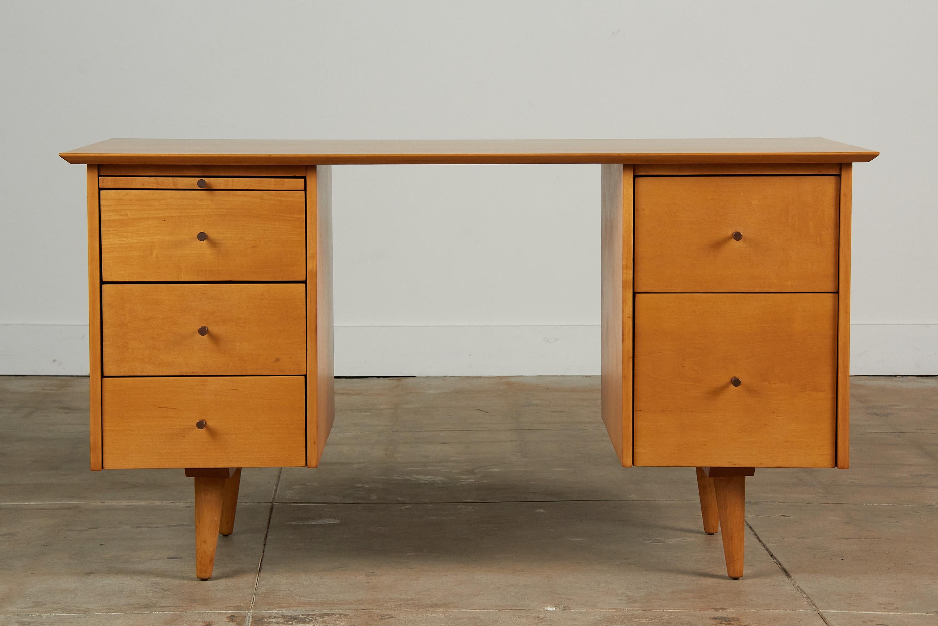 Paul McCobb writing desk from the Planner Group Collection for Winchedon, c.1950s. This maple desk features five drawers with solid brass knobs. There is a pull out writing table on the left hand side with three drawers beneath. The right ride has