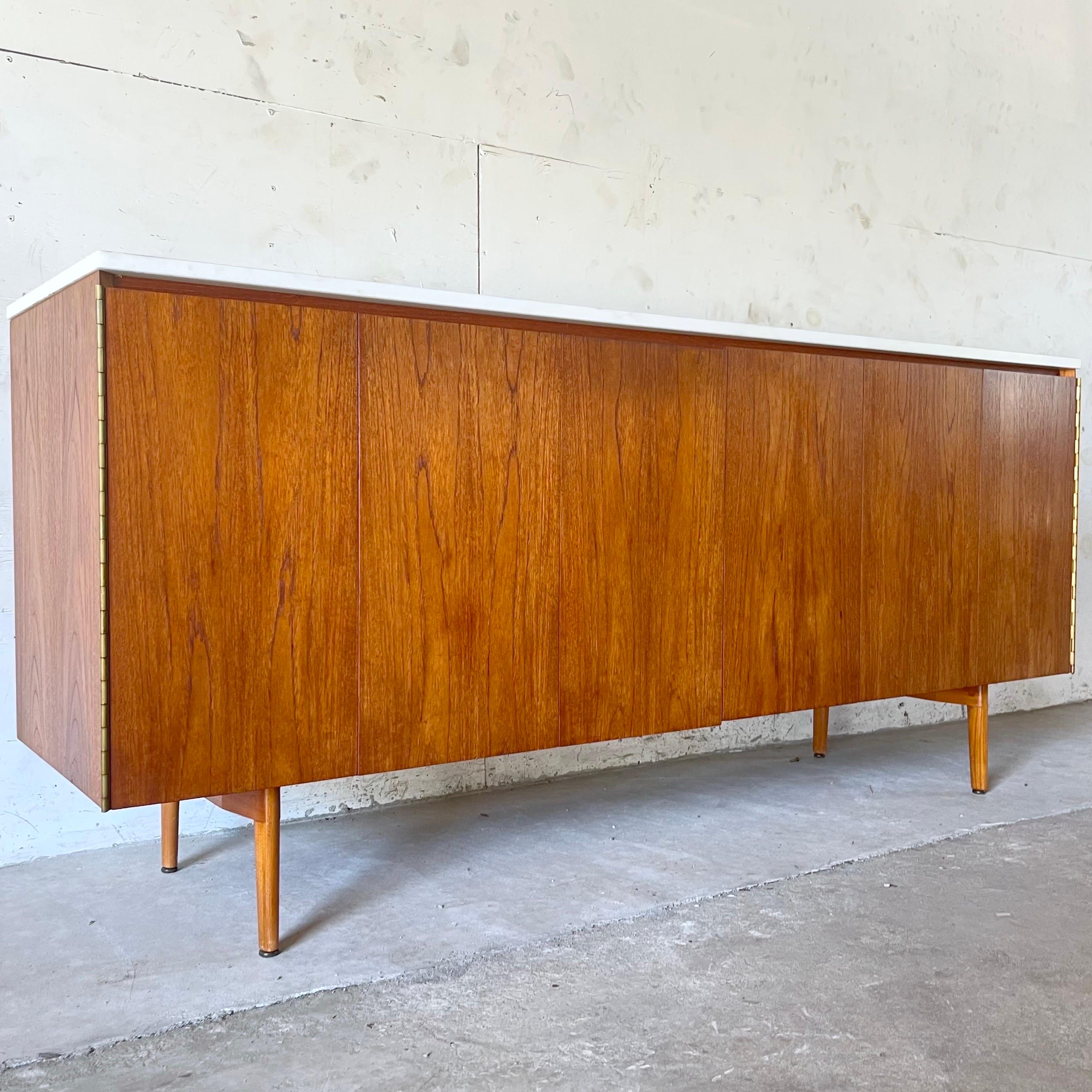 This impressive mid-century modern sideboard by Paul McCobb for Directional Furnitures Calvin Group features trifold doors that conceal spacious interior cabinets with a mix of adjustable shelf space and upper drawers. Ideal mix of storage options