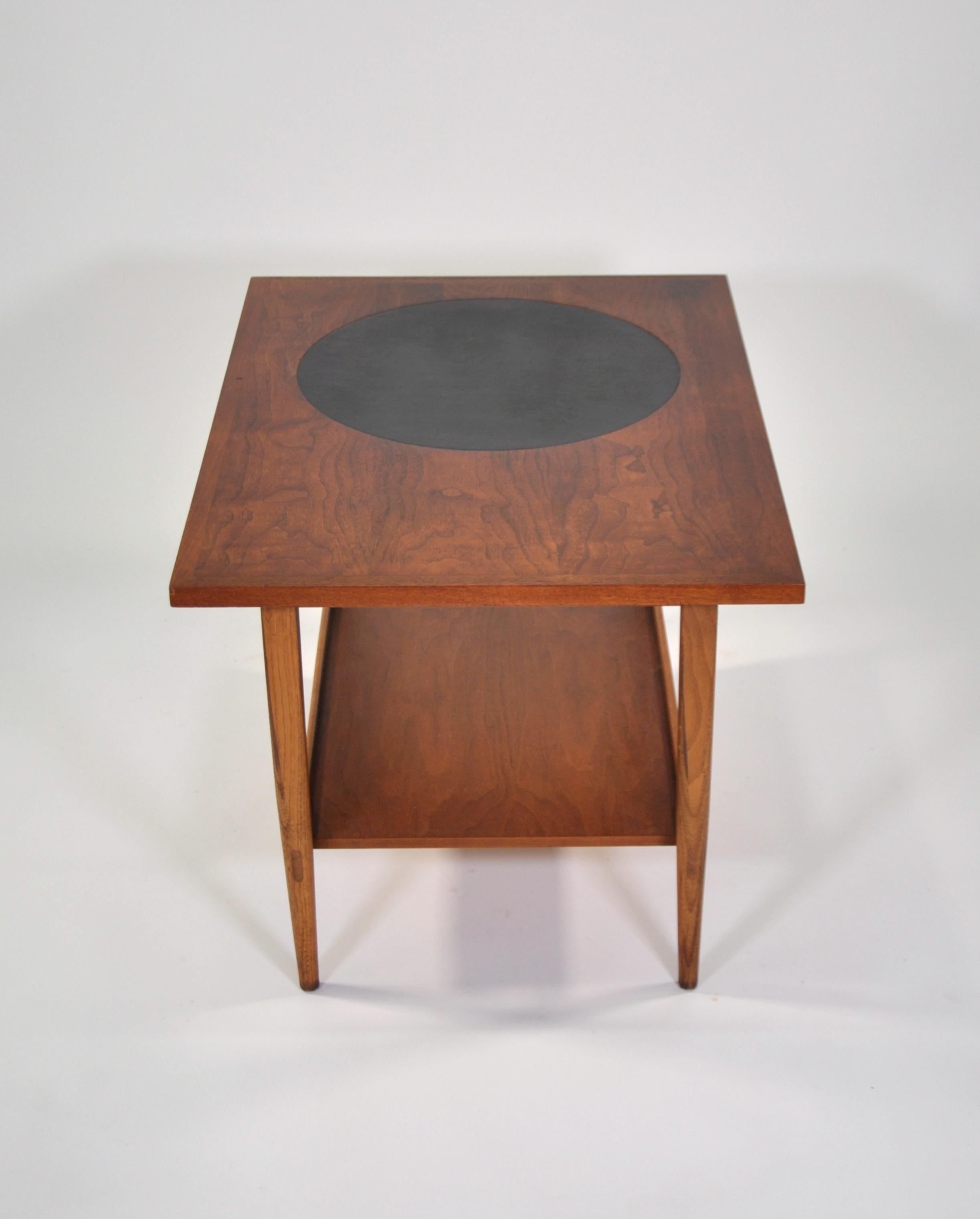 A rare vintage Mid-Century Modern end table designed for the Lane Signature collection by Paul McCobb, model 1001-05, dating from 1962. The occasional table features an inset round black leather top, highly figured grain and elegantly tapered legs.