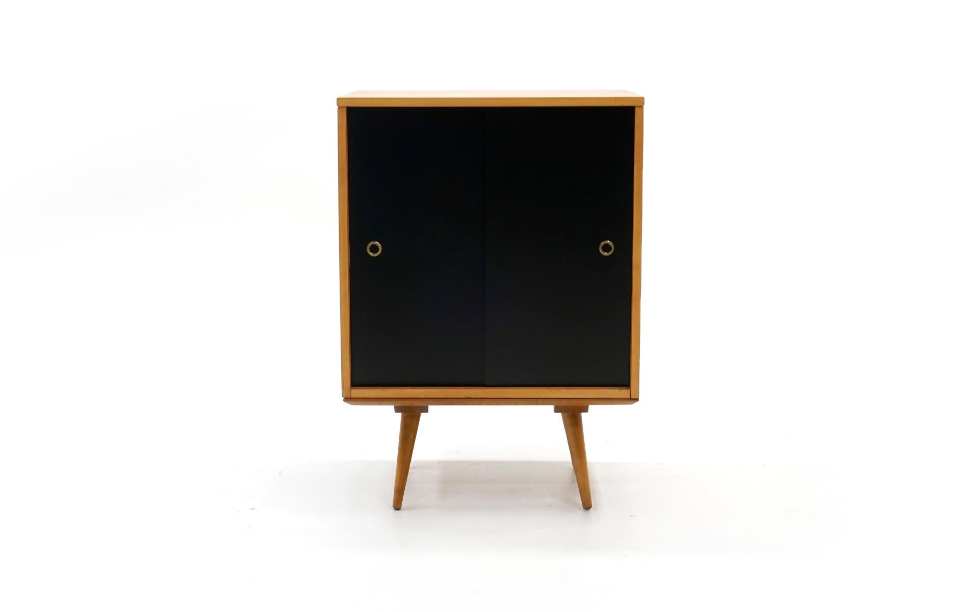 Paul McCobb Planner Group cabinet for Winchendon Furniture Company. Solid maple construction. Expertly restored. This would make an excellent media cabinet as it has black sliding doors that reveal a fixed shelf with a professionally cut hole in