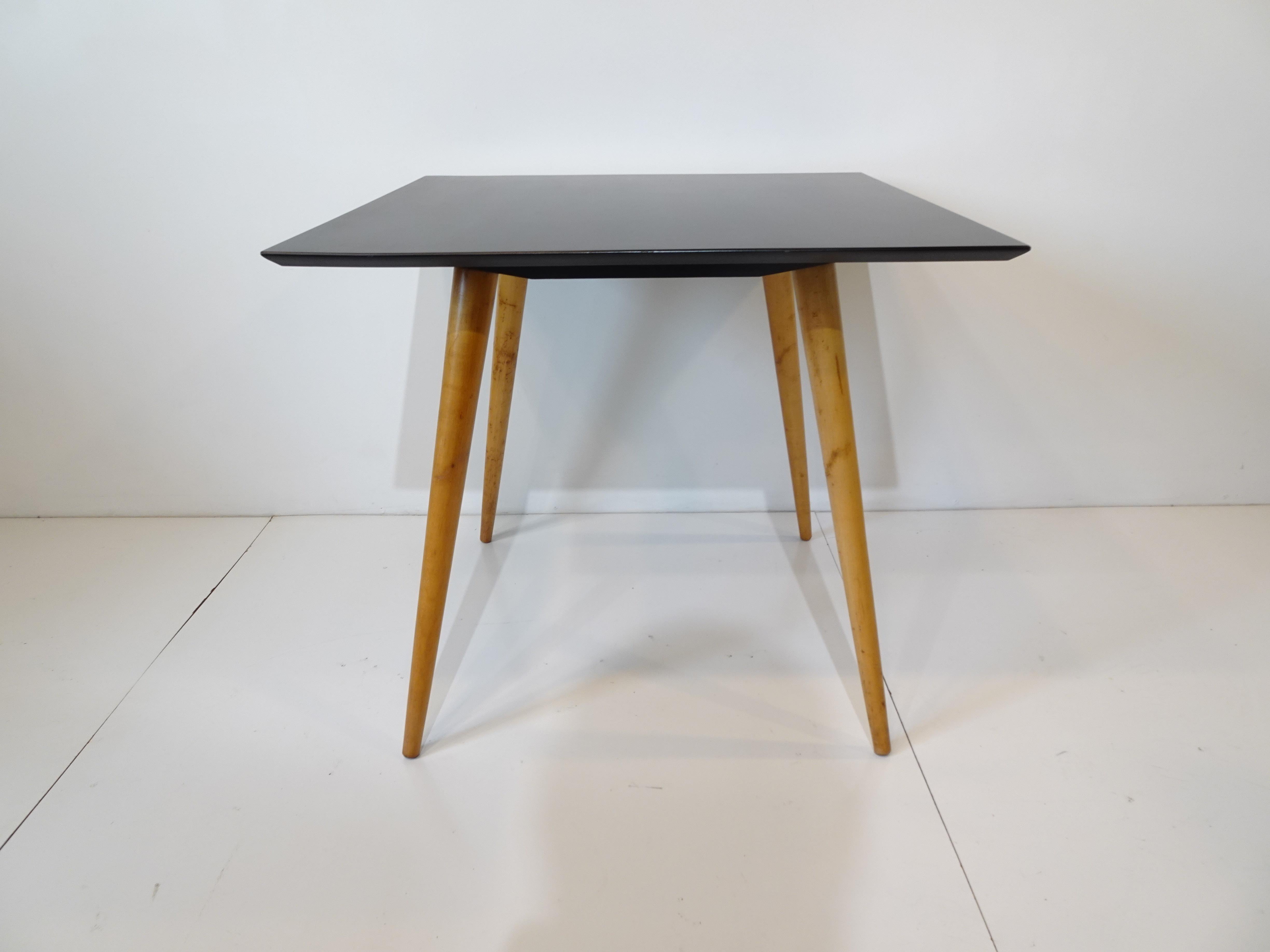A satin black topped small dining or game table with maple legs giving the piece a floating feature designed by Paul McCobb and manufactured by the Winchendon Furniture company for their Planner Group Collection.