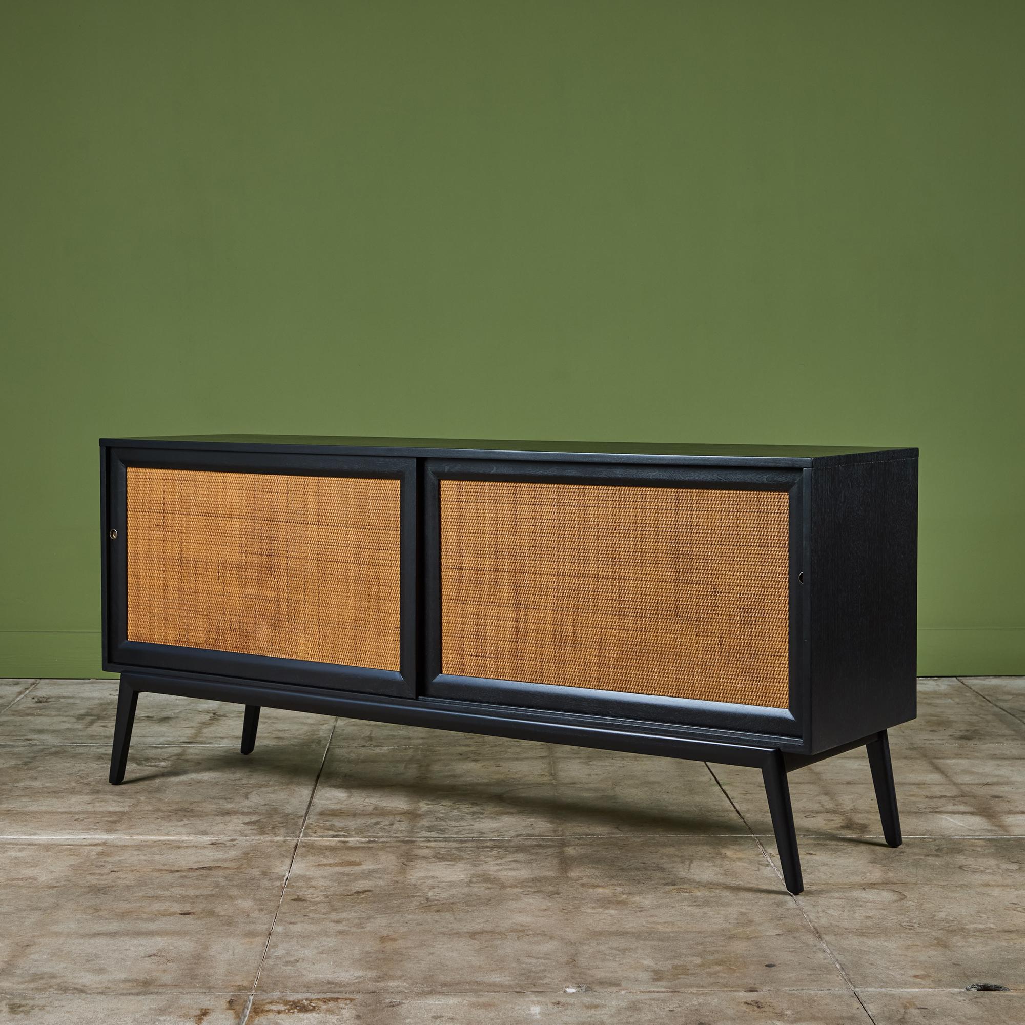 Paul McCobb style ebonized credenza with cane sliding door fronts. The interior of the piece features three drawers on one side and two shelves on the other. The contrast of the ebonized finish and tan cane door front really make this piece stand