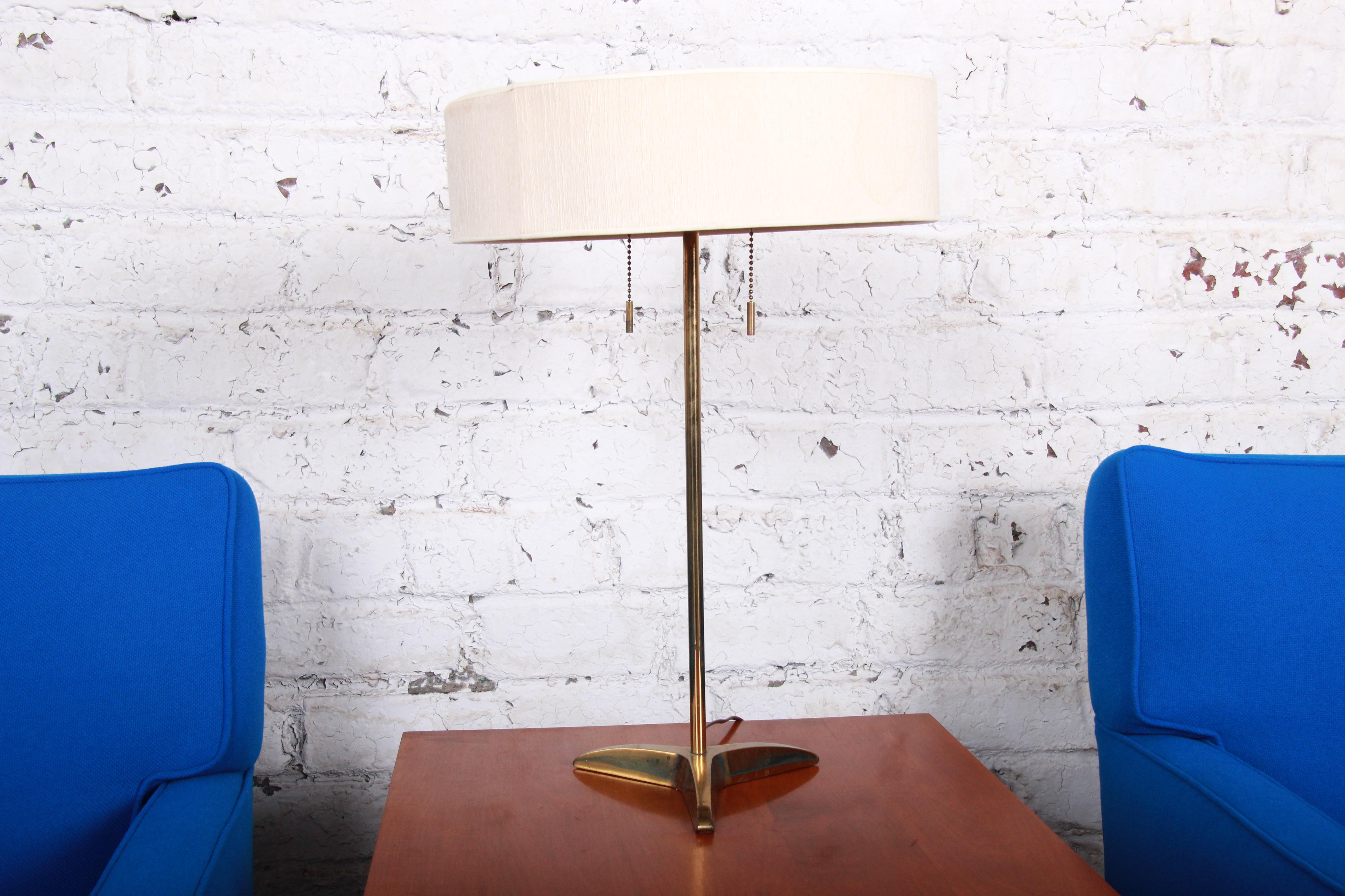 A gorgeous Paul McCobb style mid-century modern brass table lamp by Stiffel. Simple and elegant, with a three-pronged pedestal base and original round lamp shade with tassel pulls. The original Stiffel label is present. The lamp is in good working