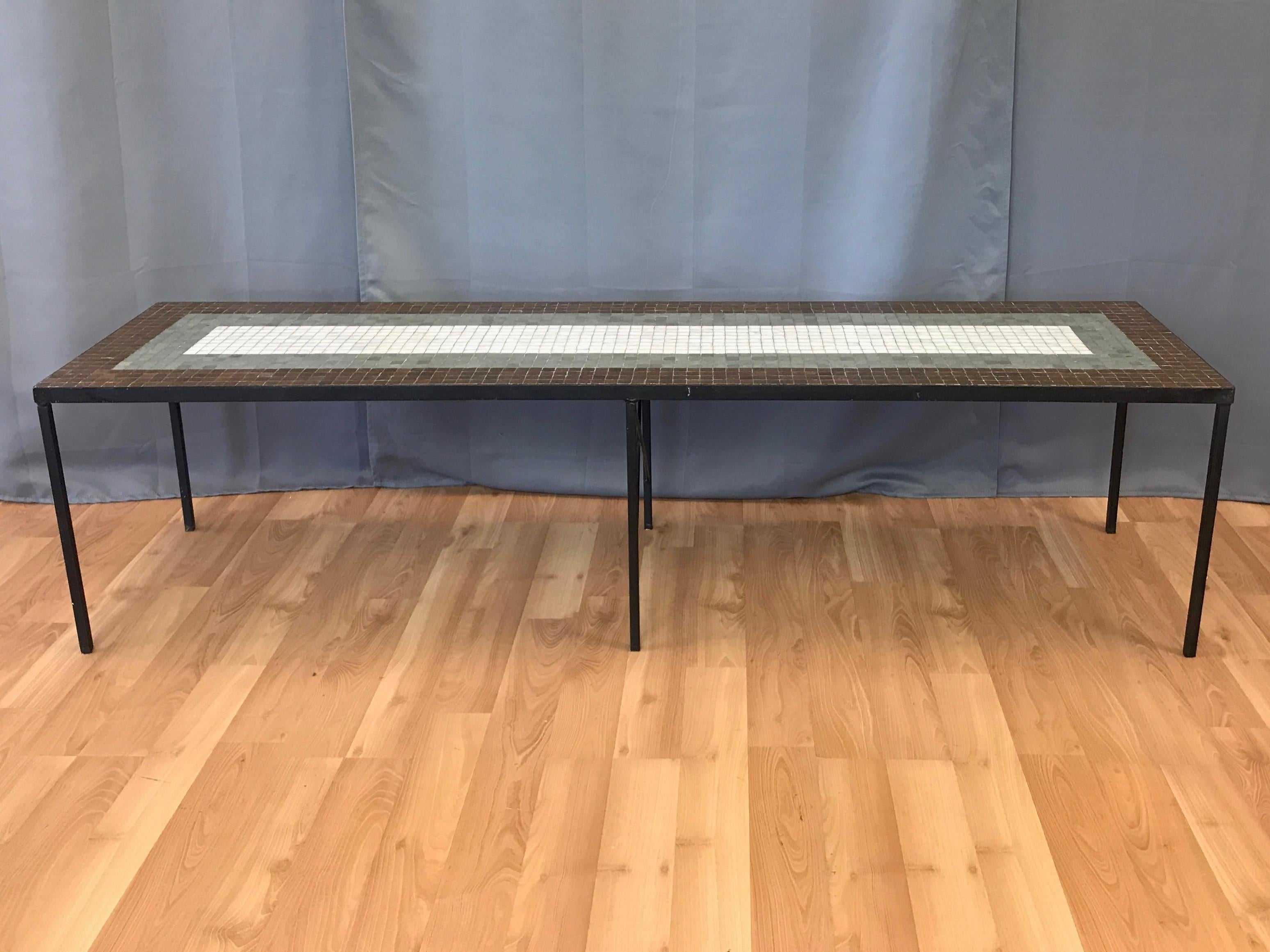 A 1960s six-foot-long Paul McCobb-style tile and iron coffee table or bench.

Very handsome top with 1” square glass tiles in white, grey, and brown affixed to wood. Satin black enameled iron frame and legs in the Minimalist style of Paul McCobb.