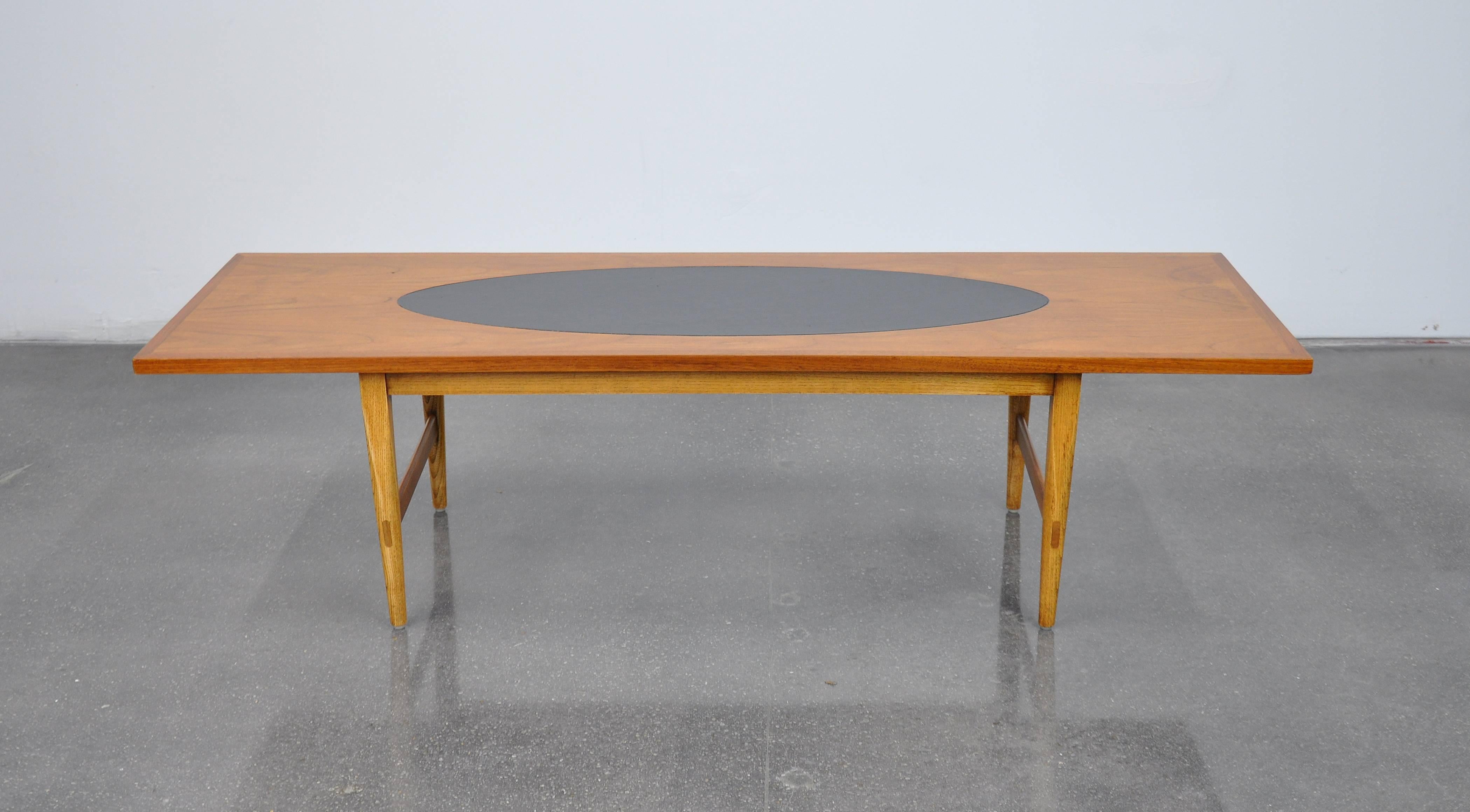 A very rare Mid-Century Modern vintage cocktail table designed for the Lane Signature collection by Paul McCobb, model 1000-01, dating from 1962. The table features an inlaid elliptical black leather top, highly figured grain and elegantly tapered