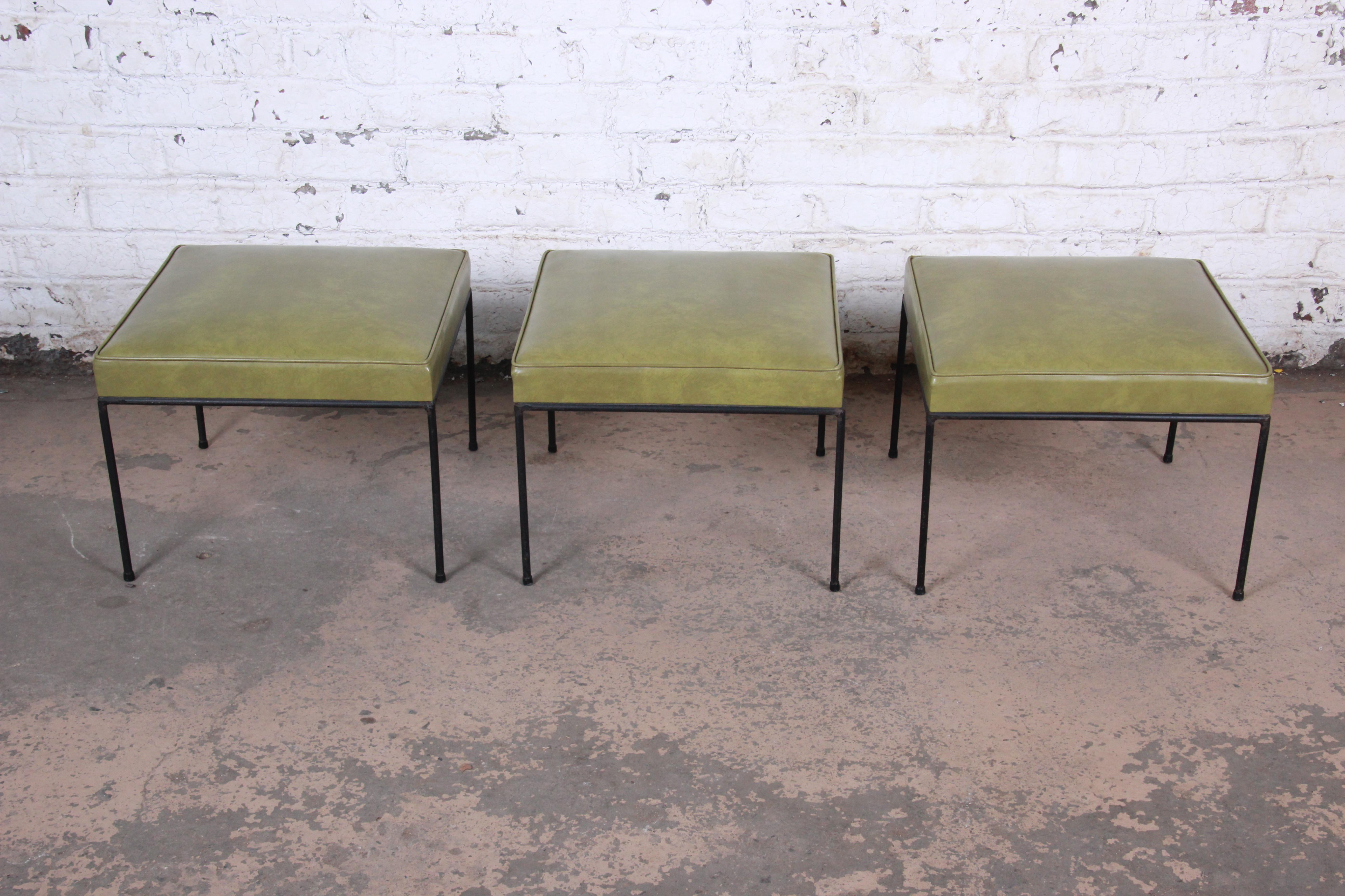 A rare set of three matching Mid-Century Modern stools or ottomans designed by Paul McCobb. The stools feature nice black iron legs with all feet glides still intact. The green vinyl upholstery is original. An excellent example of McCobb's