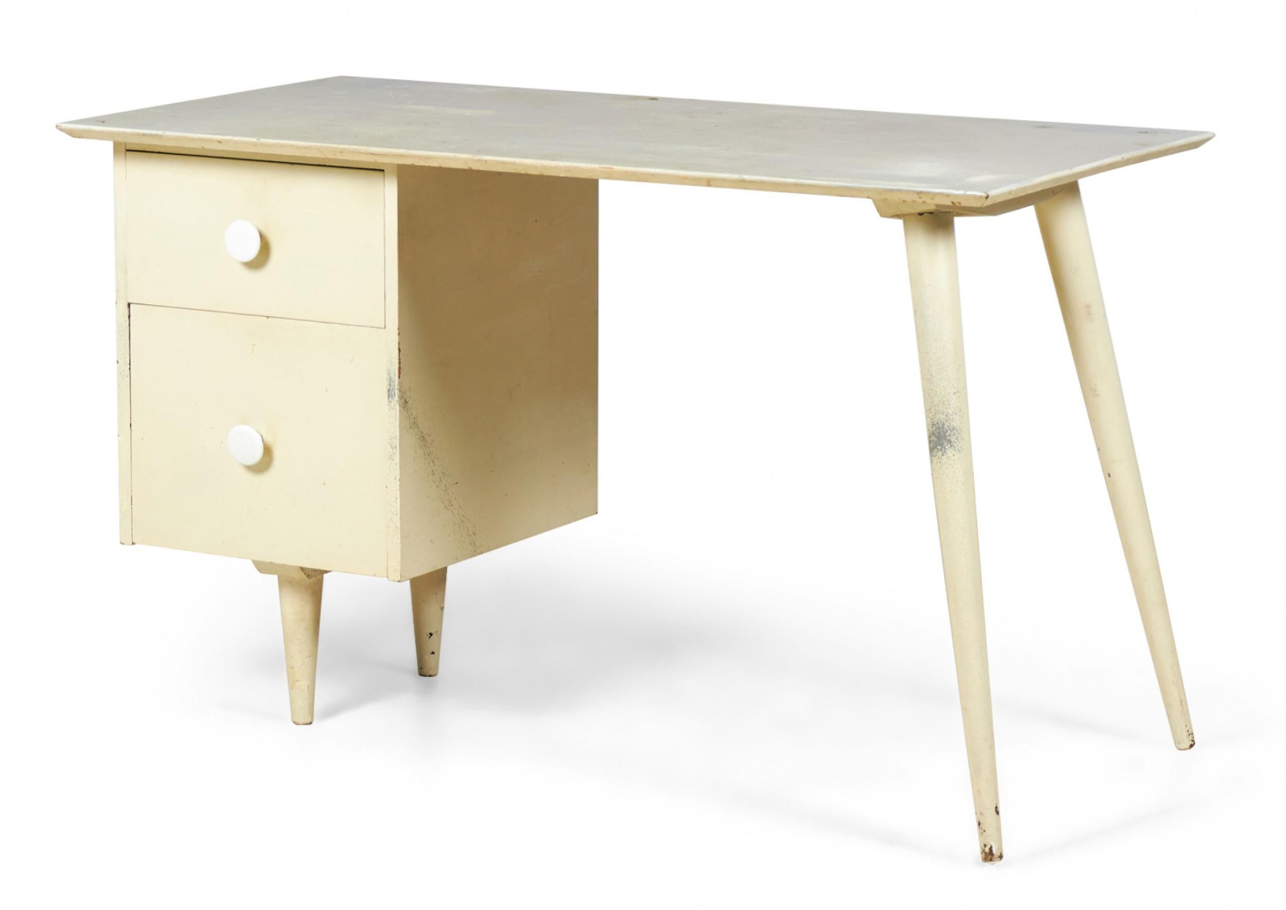 American mid-century wooden white-painted student desk with a rectangular desktop supported on the left by two drawers with circular knob pulls resting on two short tapered legs, and on the right by two angled tapered legs. (PAUL MCCOBB, model 1560)