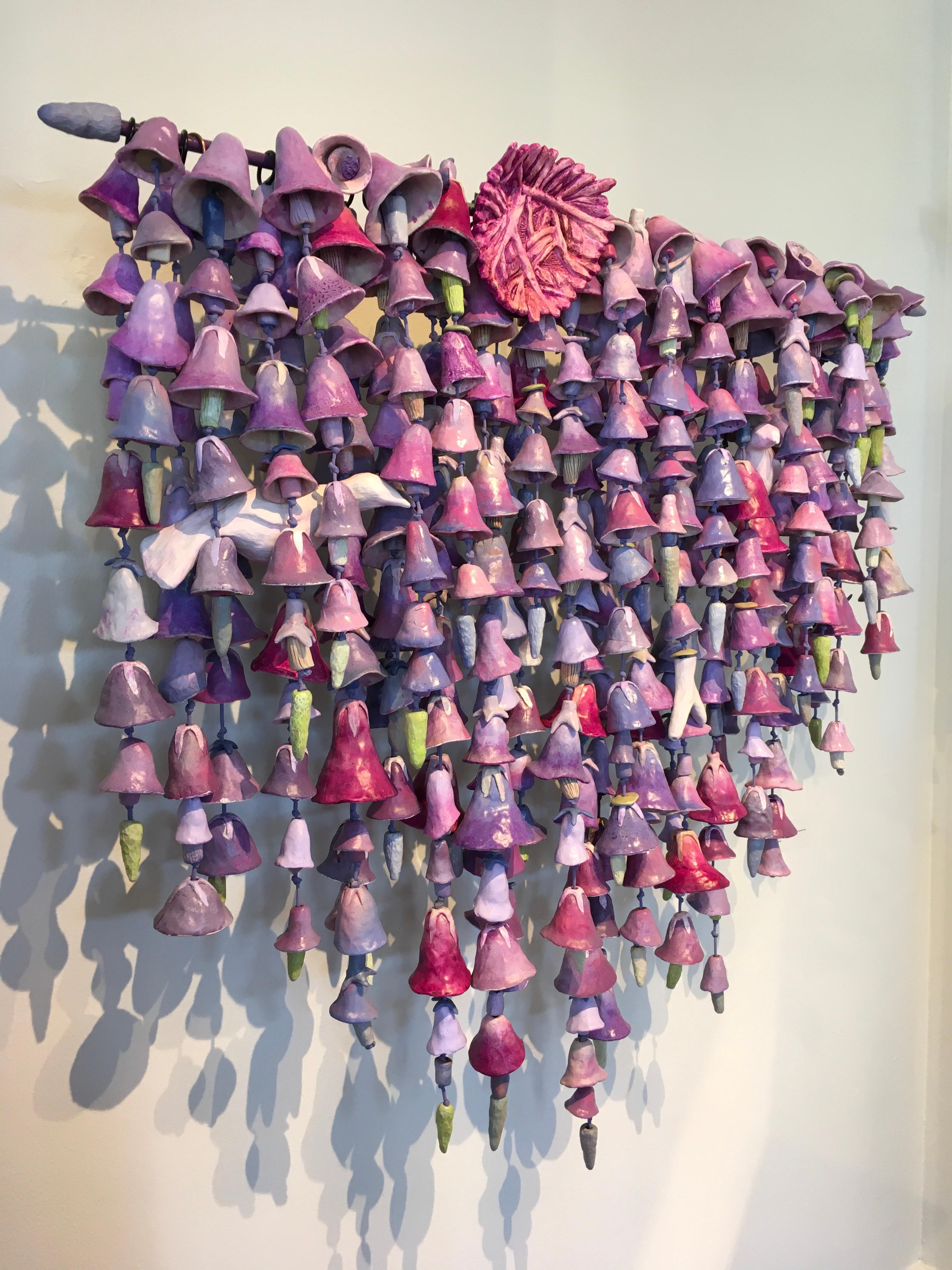 This ceramic sculpture, 'A Safe Place to Stay, by Paul Medina comprises many strands of fired-clay forms linked by nylon cord that hang from a steel rod bracketed to the wall. 
Shades of lavender, pink, gray and green are the predominant colors of