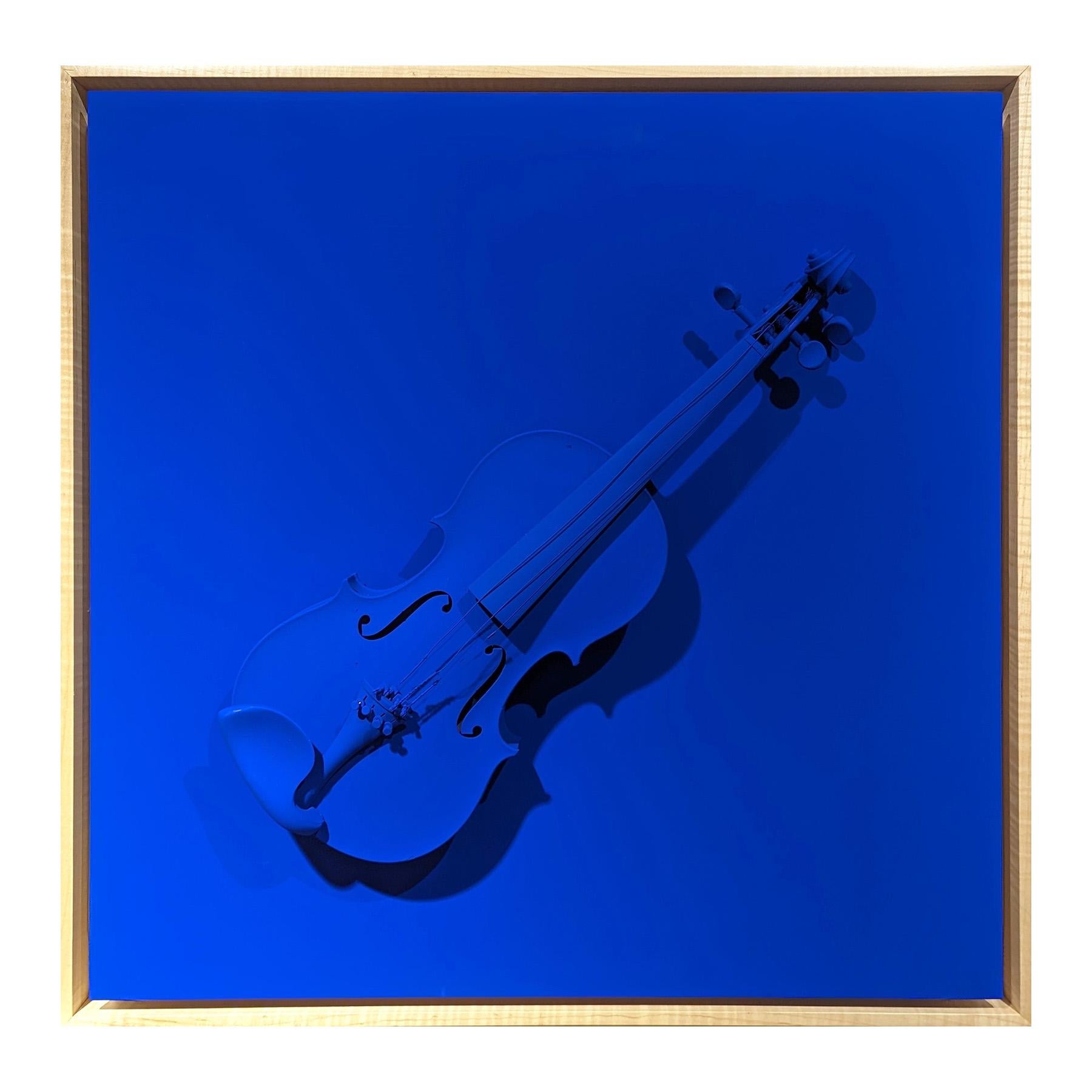 Bright blue sculptural painting by contemporary artist Paul Reeves. The work features a found violin painted blue floating against a background of the same vibrant blue color. Currently hung in a light wood floating frame.  

Dimensions Without