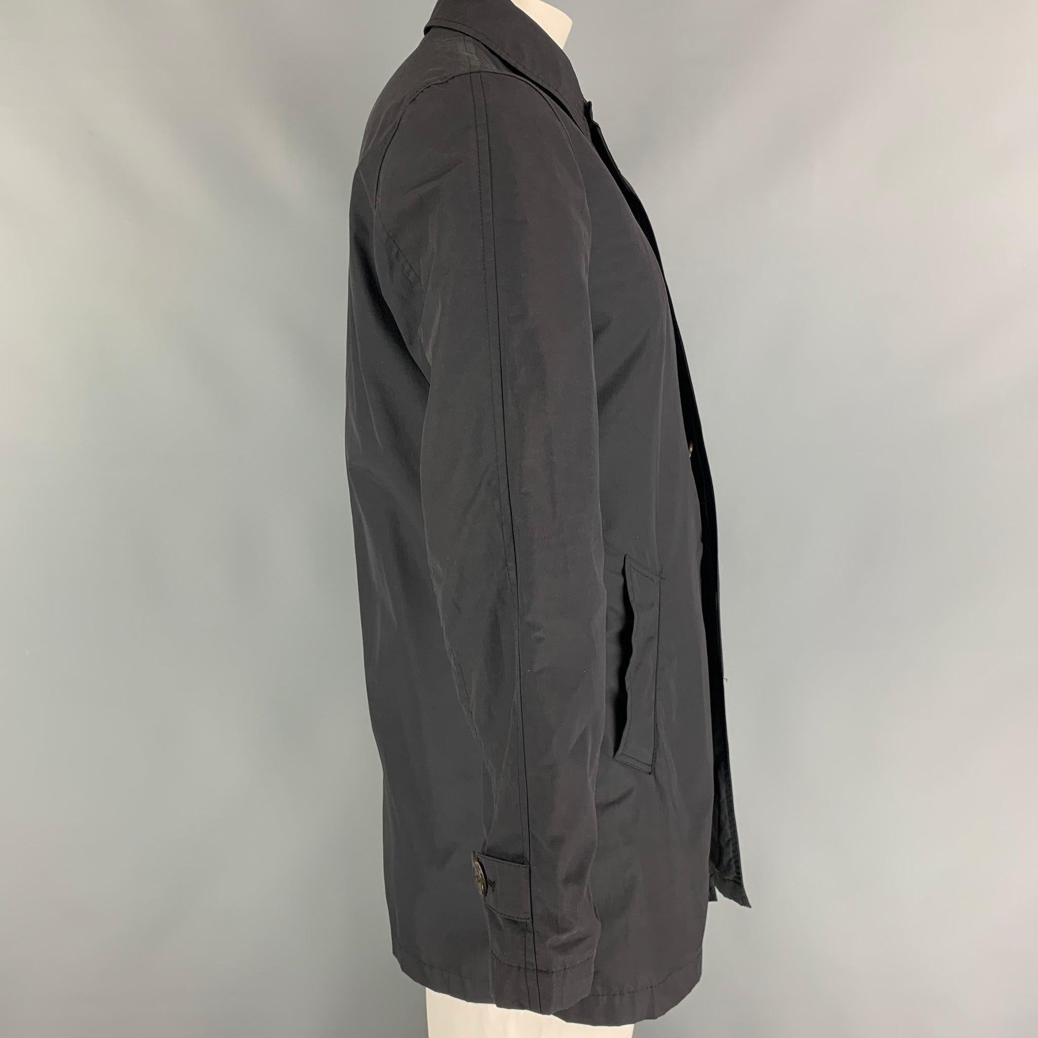 Paul Smith black trench coat style jacket comes in a nylon fabrication with blue cotton interfacing.Features include welt pockets,tone on tone buttons,and shirt collar.Made in Lithuania.Excellent Pre-Owned Condition.  

Marked:   Size Medium