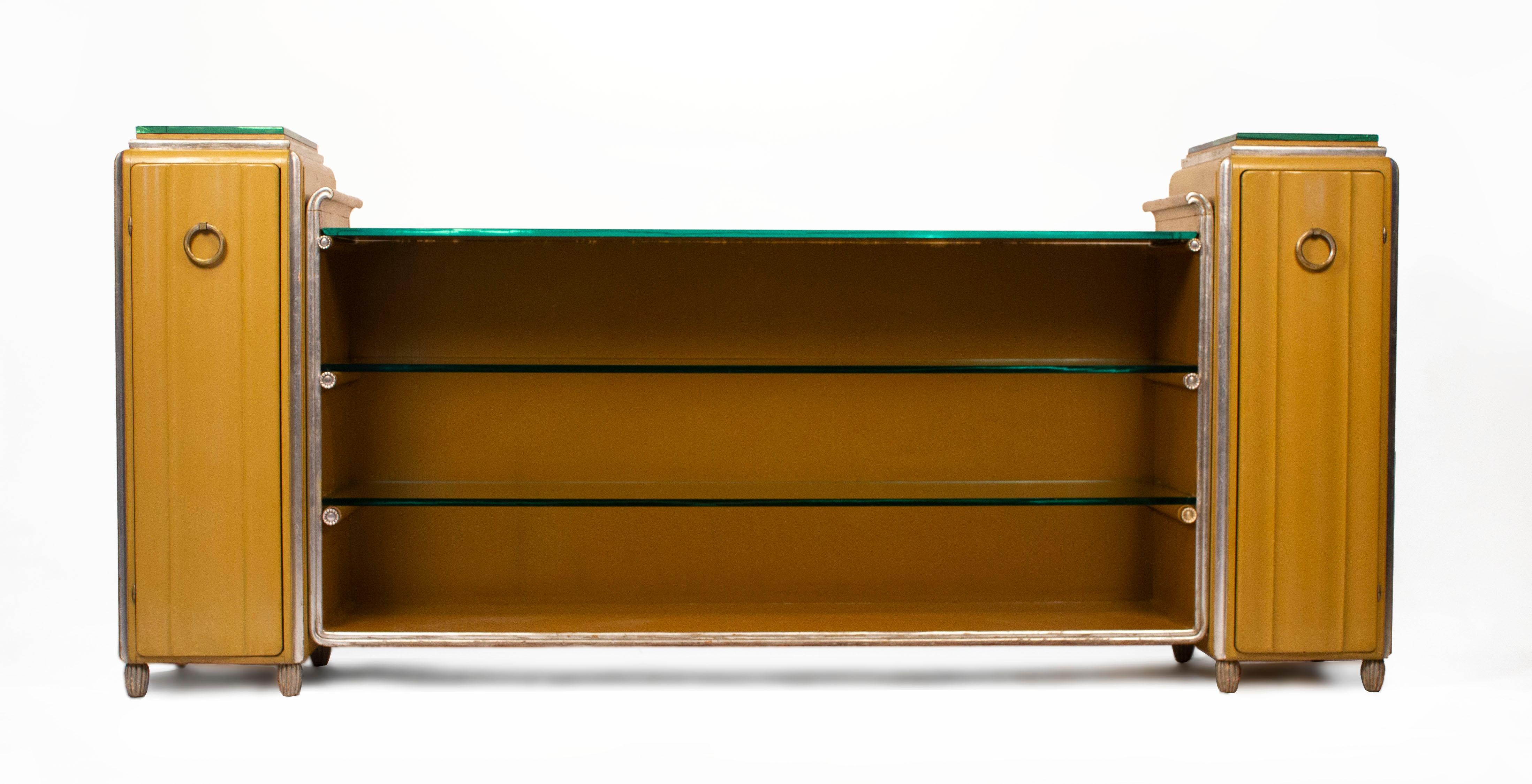 Rare and important lacquered sideboard in two tone yellow ochre finish with silver leaf ornamentation, original mirrored tops, glass shelves, bullet hinges, faceted solid brass silver leafed hardware and silver plated shelf ornamentation. This