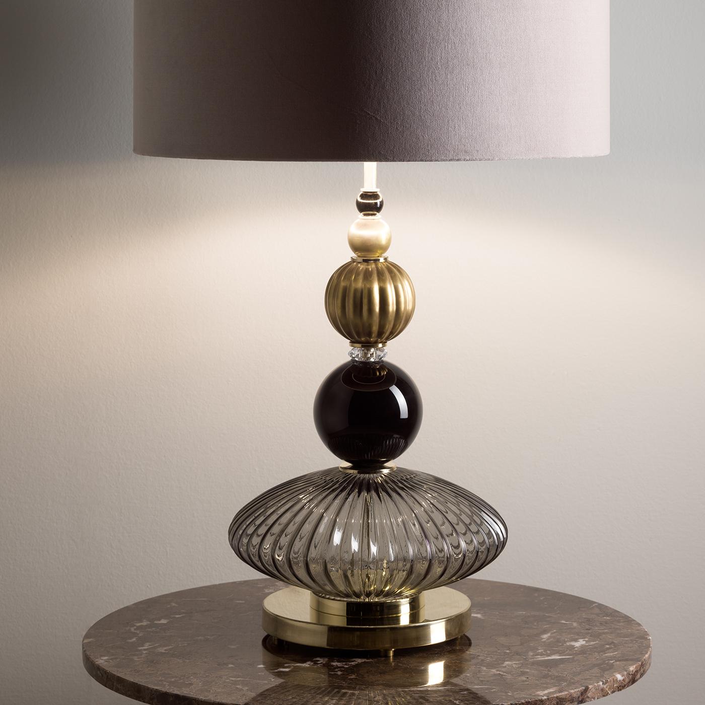 A series of glass elements of different shapes stacked one on the other forms the eye-catching stem of this exquisite table lamp. Each element boasts a different color and texture to add a refined sense of movement to this piece, topped with a
