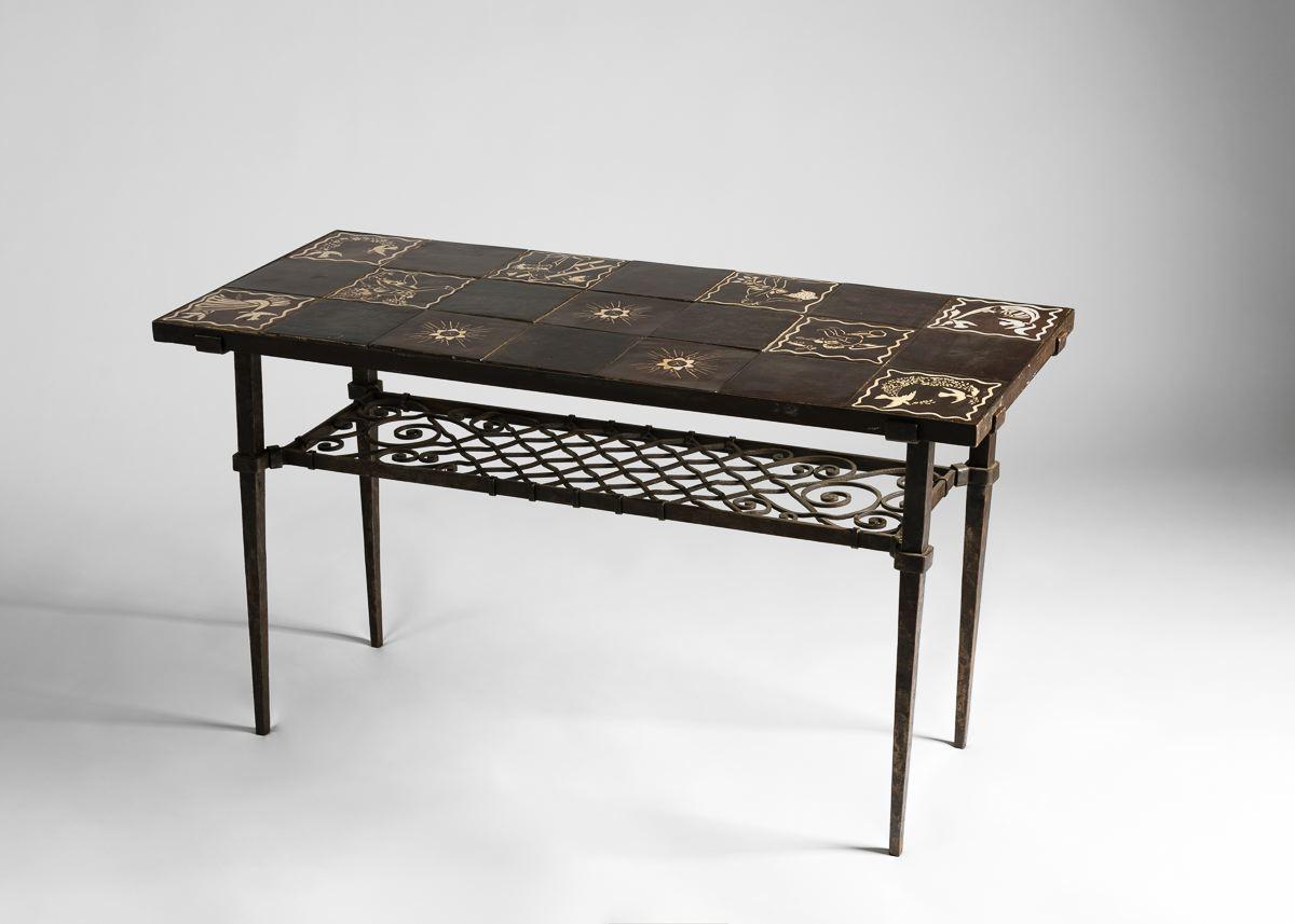 This long side table has a ceramic top assembled from tiles created by the master ceramist Paul Vera, each depicting a fanciful vignette or design and glazed in black and white. The base, in wrought iron, is assembled of long thin legs, and