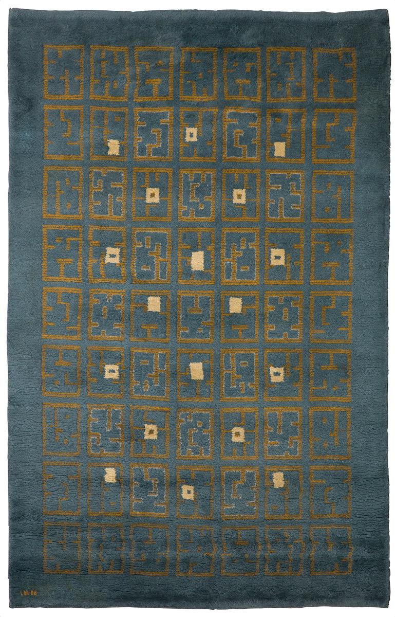 A knotted woollen rectangular rug with blue ground, central decoration forming a geometric composition with ochre and beige Aztec designs. Signed 
