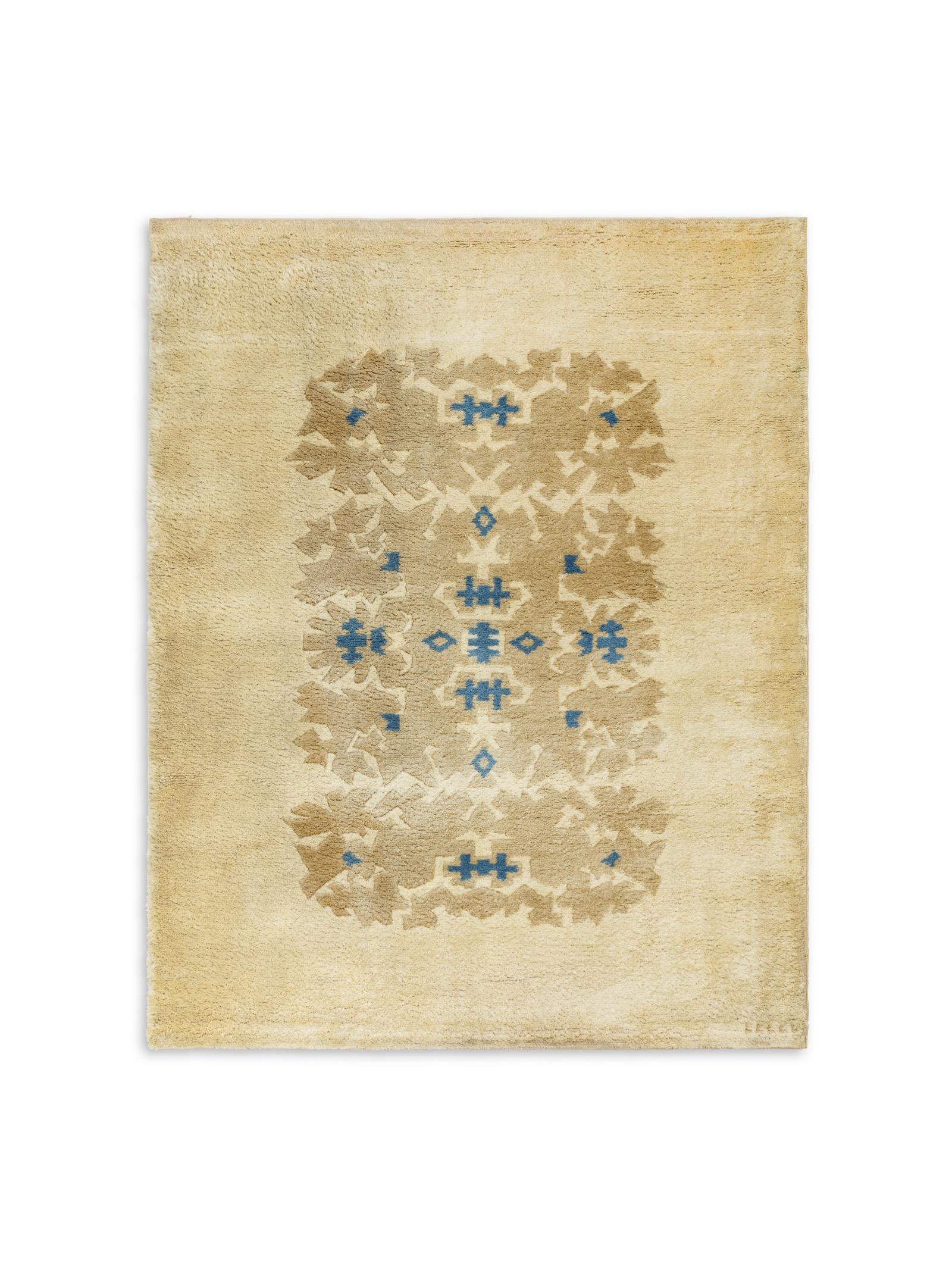 A rectangular knotted woolen rug with stylized blue and dark beige decoration on a beige background. Signed in the frame.