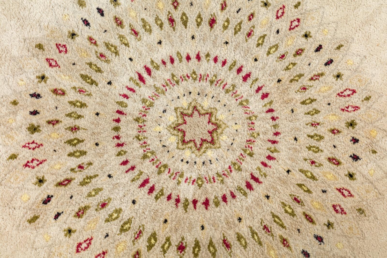 A round knotted woollen rug with beige ground and yellow border, radiant decoration of red, green and yellow carved rhombuses, central medallion in the shape of a star finished off with a red edge. Signed 