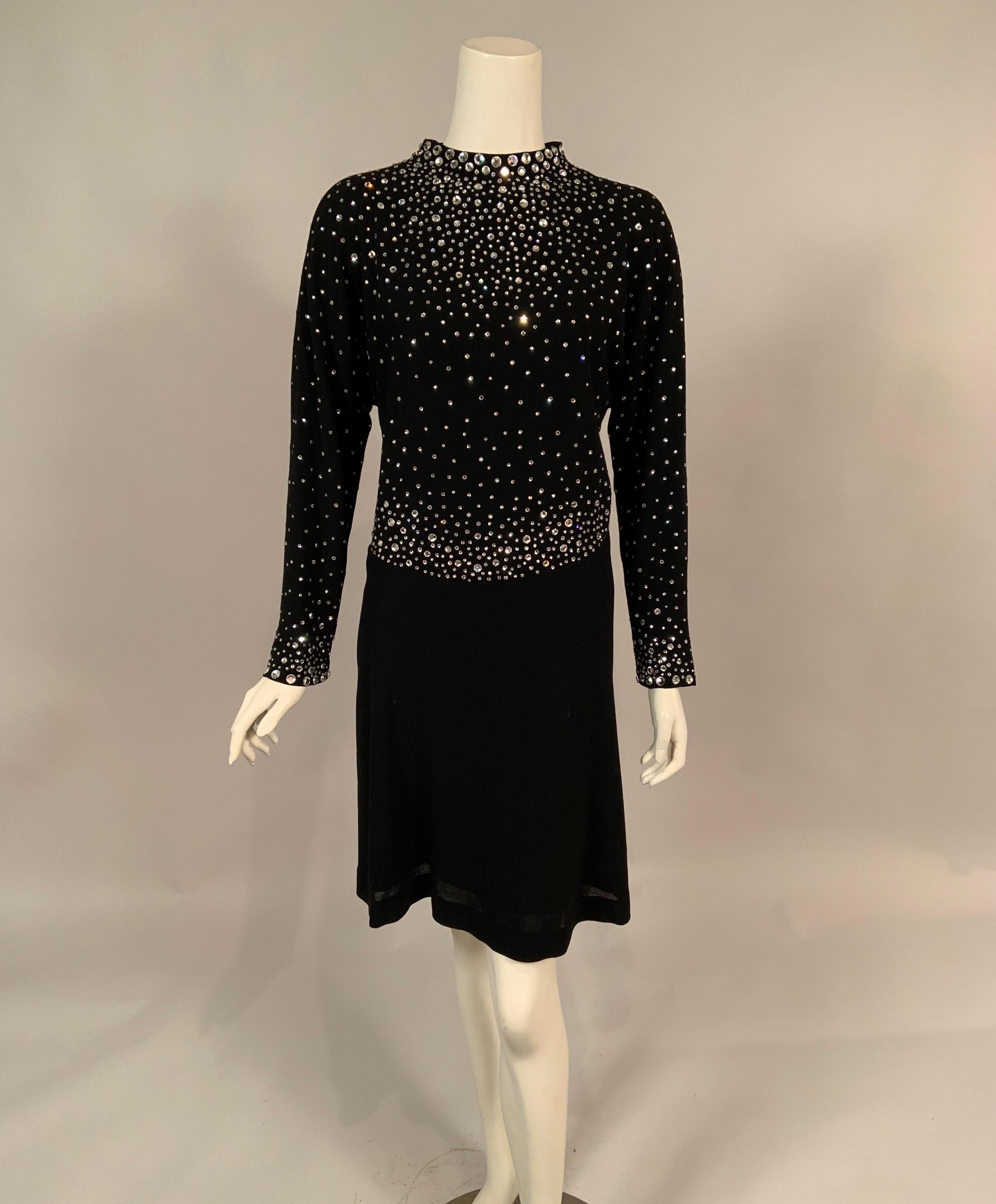 Pauline Trigere loved the look of these prong set rhinestones and used them repeatedly on coats and dresses throughout her career.. This example is a lightweight black wool crepe dress with a round neckline, long sleeves and a center back zipper.