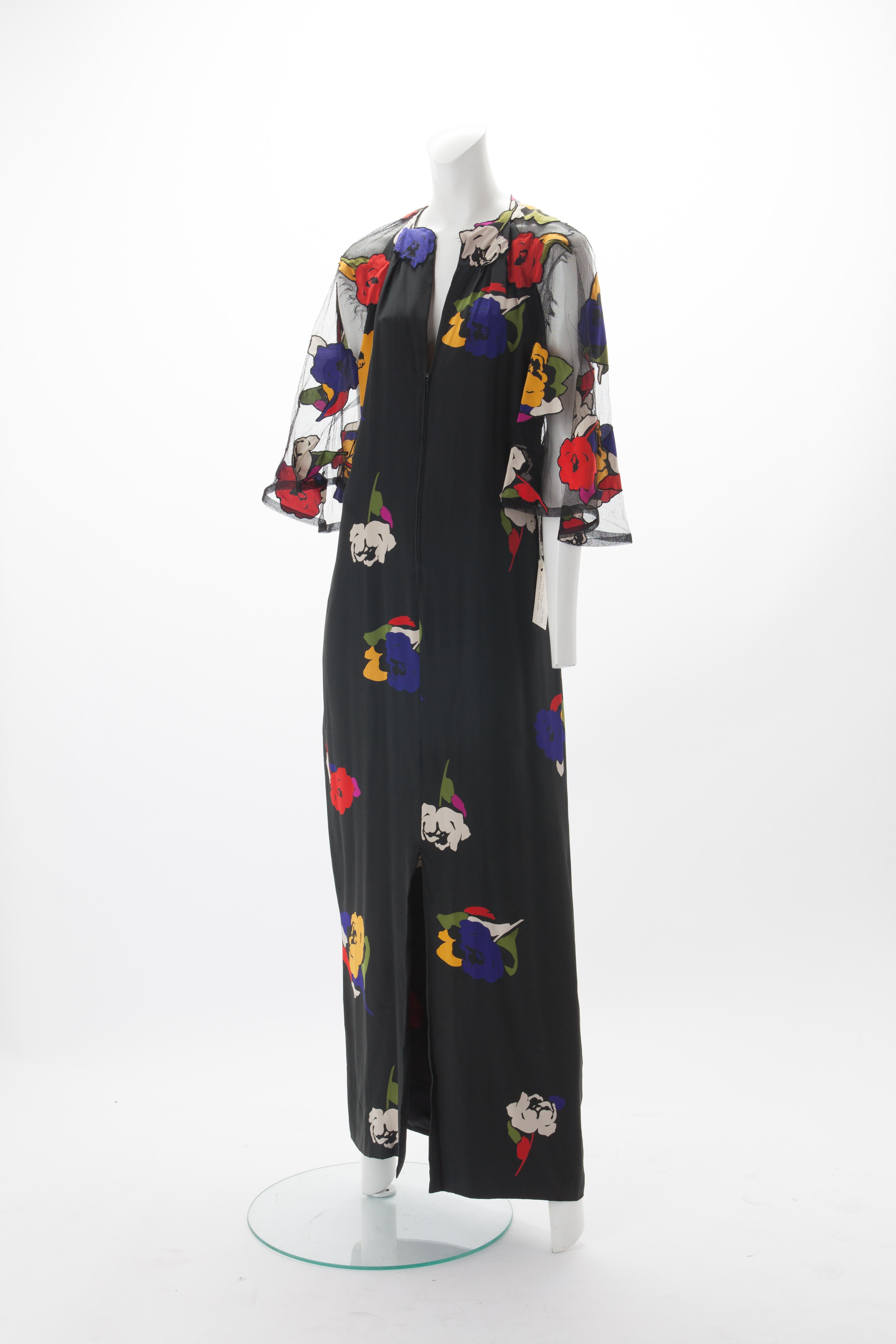 Pauline Trigère Silk and Net Gown with Floral Appliqués c.1970s.
Full length flowy dress with net bell sleeves and floral silk appliqués. Zipper at neckline and slit at center front. Features low-cut net back.   
Fits US 4 to 8. 