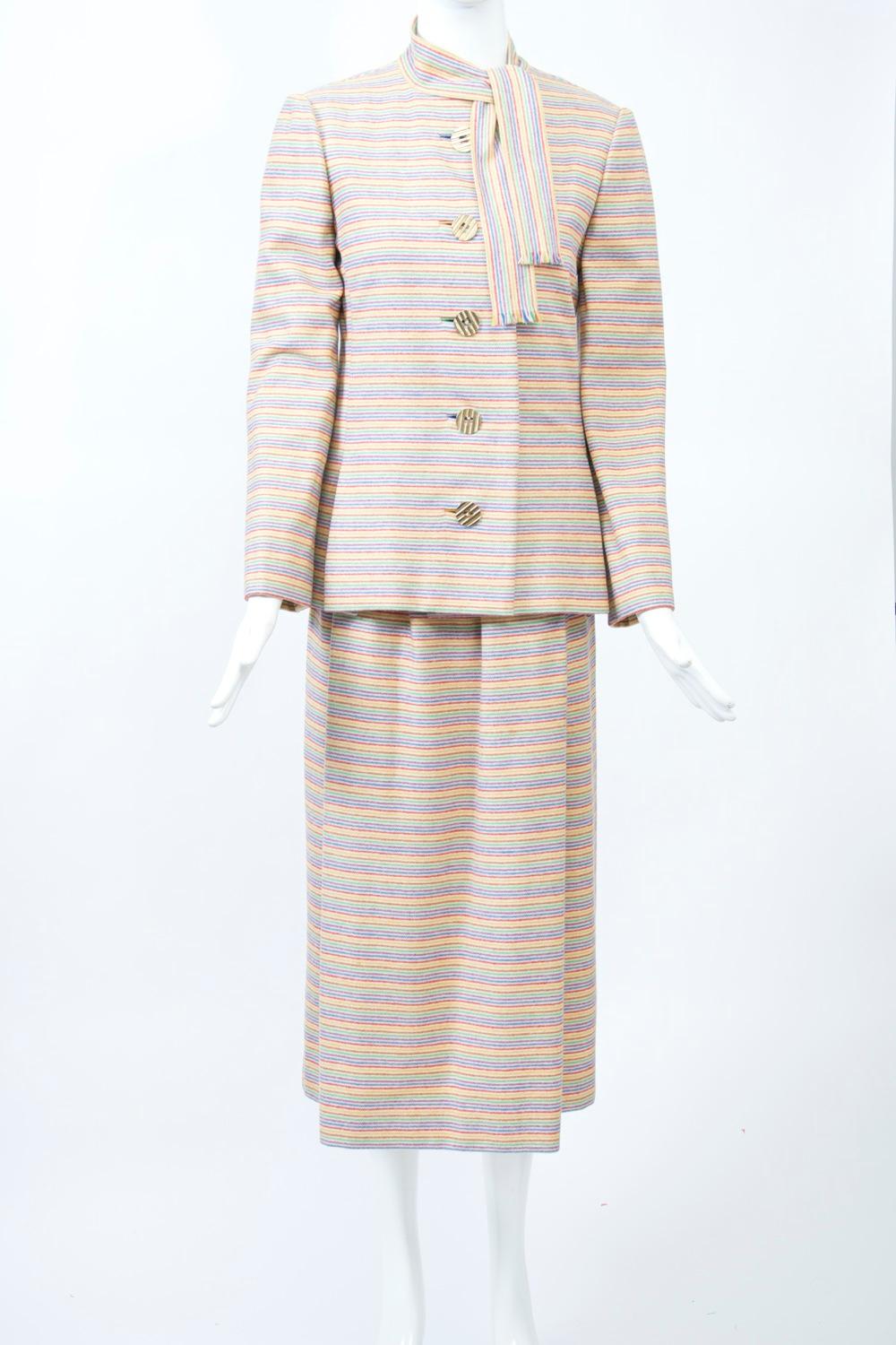 Typical Trigère elegance and workmanship define this 1970s suit in soft wool featuring narrow, horizontal rainbow stripes on an ivory ground. The single-breasted jacket is long and slightly shaped with a tie neck and single pleats towards the sides,