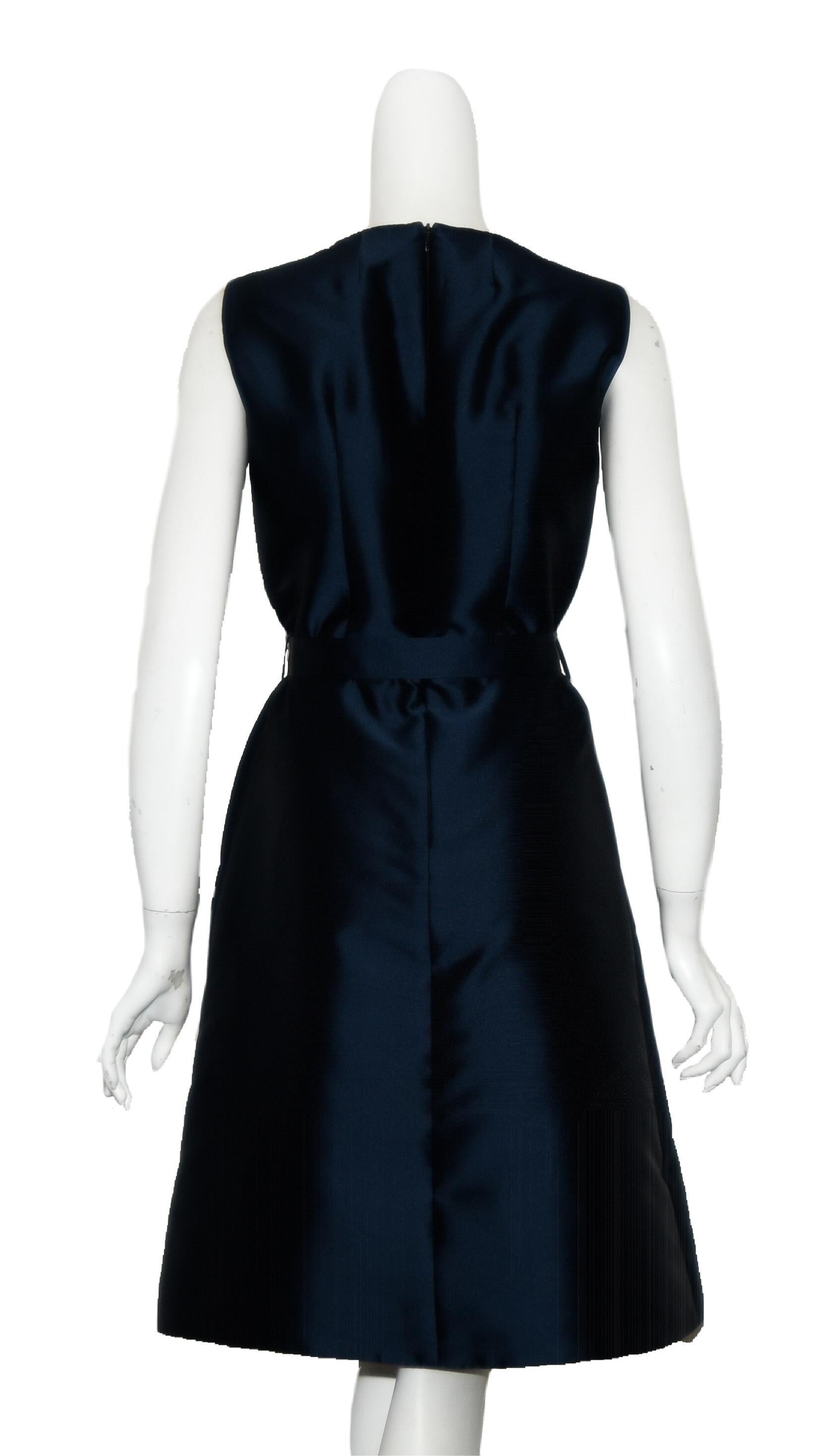 Pauw dresses start by translating an idea into a real silhouette, for real women.  This blue satin dress is cinched at the waist and slightly gathered with a flowy skirt to just below the knee.  This dress has at the neckline 2 open decorative