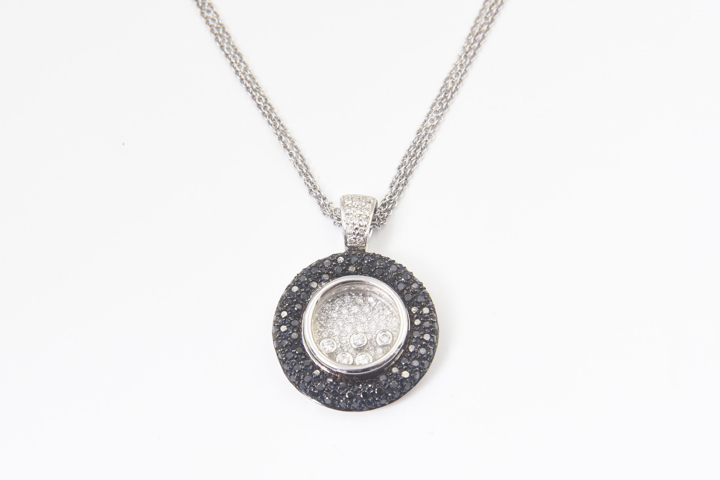Pendente a forma di cerchio con diamante di ottima fattura, caratterizzato da una cornice esterna di diamanti neri con pavé e da un centro di diamanti interni con 5 diamanti fluttuanti incastonati all'interno di una cornice di vetro.  Il ciondolo ha