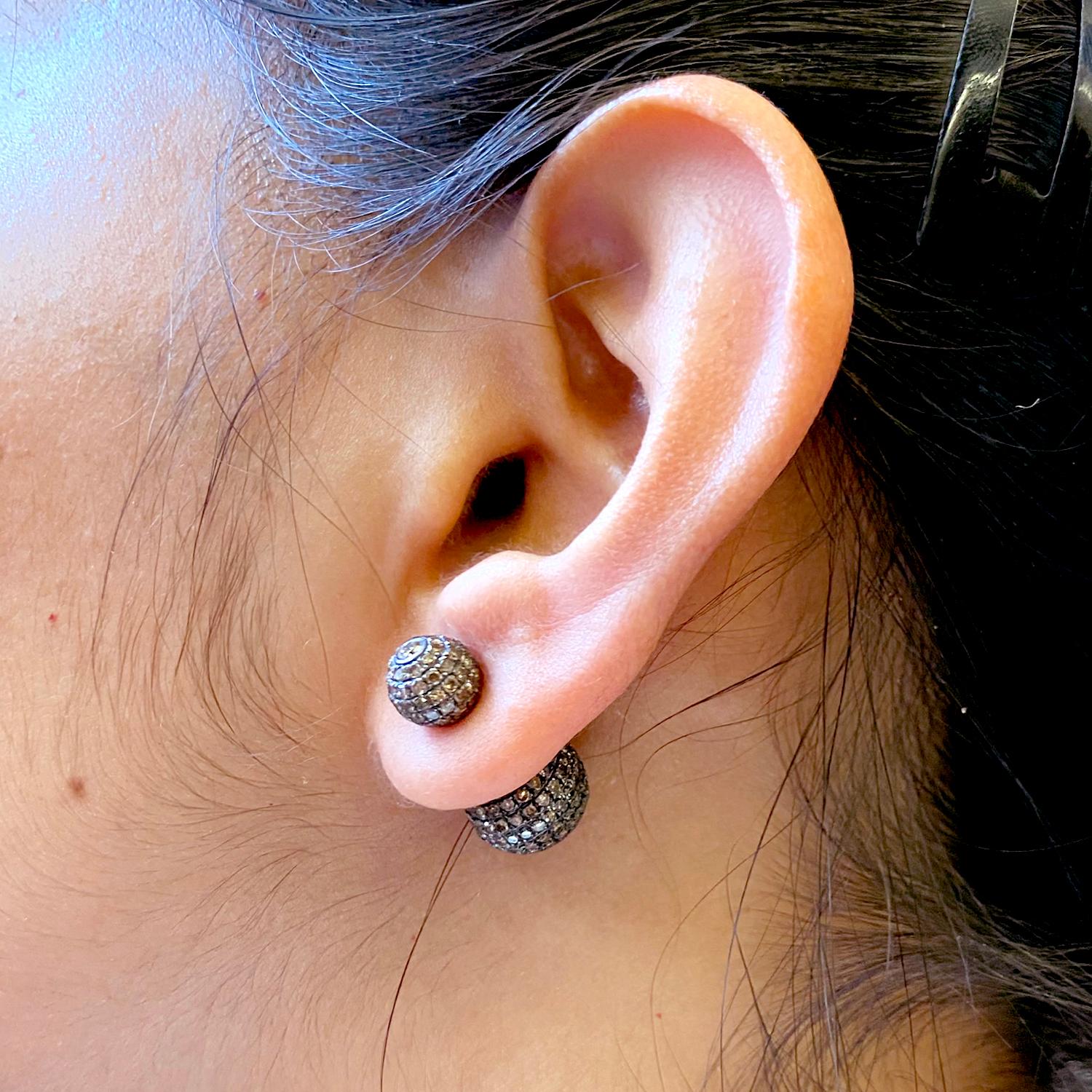 The earrings feature a round ball shape, encrusted with sparkling diamonds in a pave setting. These earrings a tunnel design, which allows them to be worn through the earlobe for a stylish and modern look. These earrings are perfect for dressing up