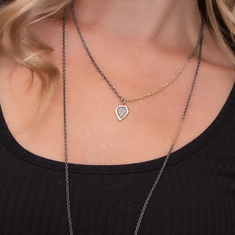 Pave diamonds fill this gold shield pendant. Based off of Victorian shields, it is a perfect piece to layer with other charms. This design pairs well with our larger diamond shield pendant. It hangs off of a blackened silver chain with inserts of