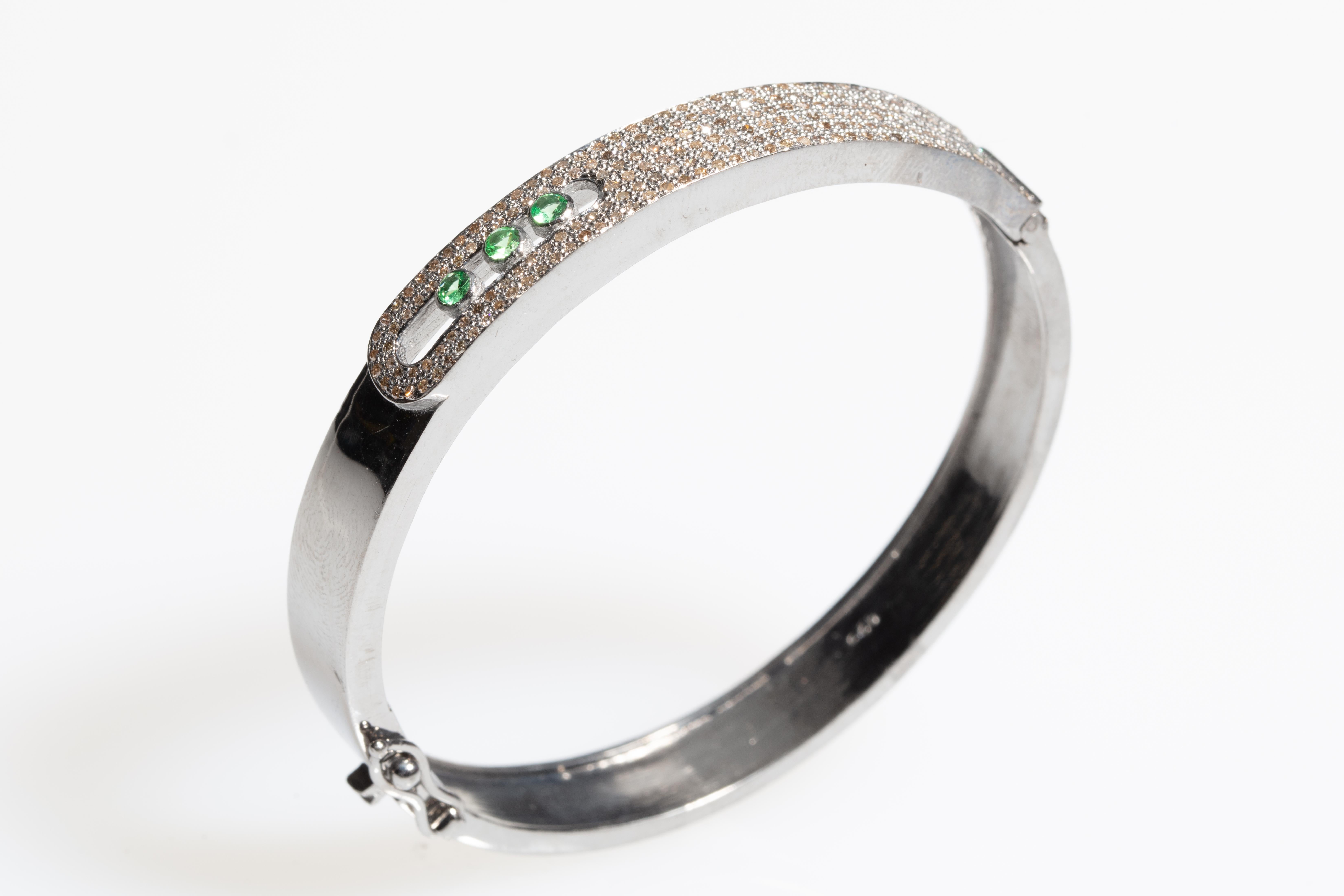 Pave`-set brilliant cut diamonds along the top of the sterling bracelet with three floating, faceted round tsavorite stones.  Push clasp with a side safety.  Oval shape keeps the stones sitting on top of the wrist.  Inside circumference is 6.5