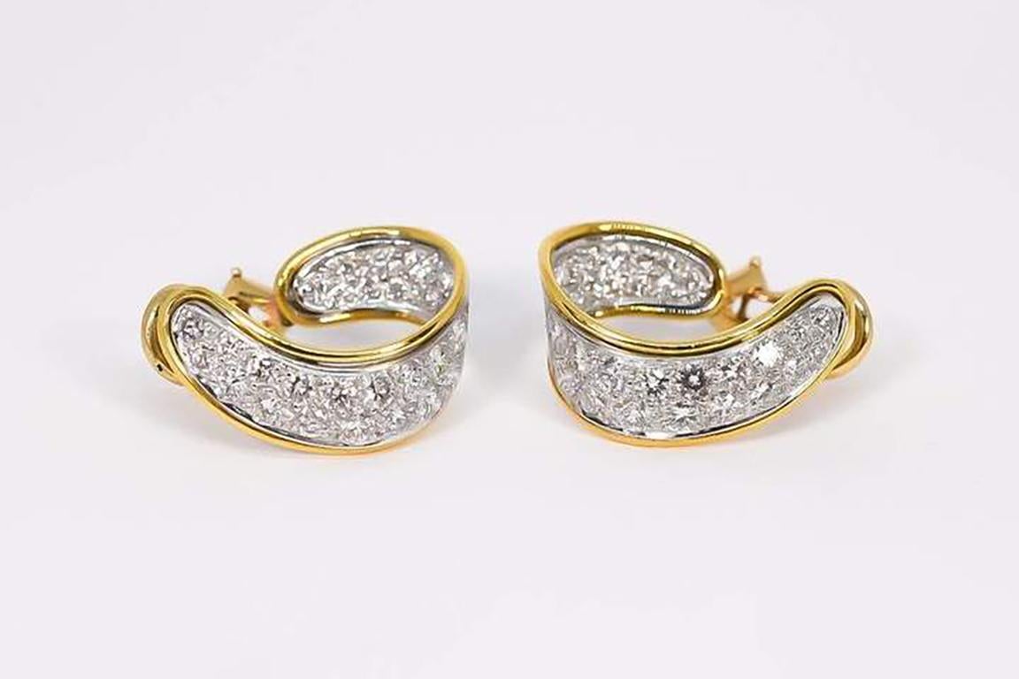 Unique pave diamond hoop earrings designed in 18 karat white and yellow gold. Ribbon loop shape with post and omega clip backs. The diamonds are pave set in white gold with yellow gold grooved edges. The earrings taper from 4.00 mm to 8.00 mm and