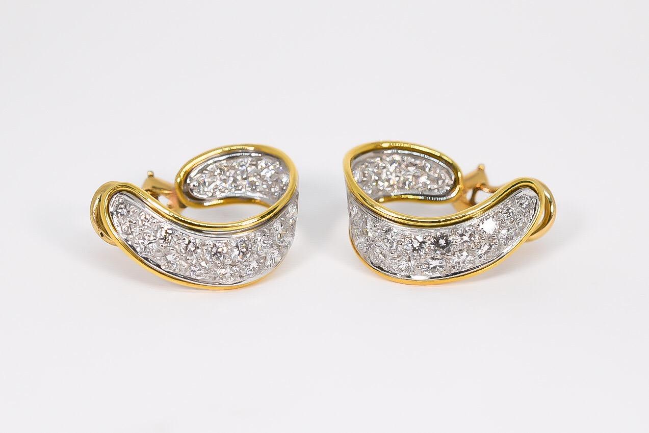 Unique pave diamond hoop earrings designed in 18 karat white and yellow gold. Ribbon loop shape with post and omega clip backs. The diamonds are pave set in white gold with yellow gold grooved edges. The earrings taper from 4.00 mm to 8.00 mm and