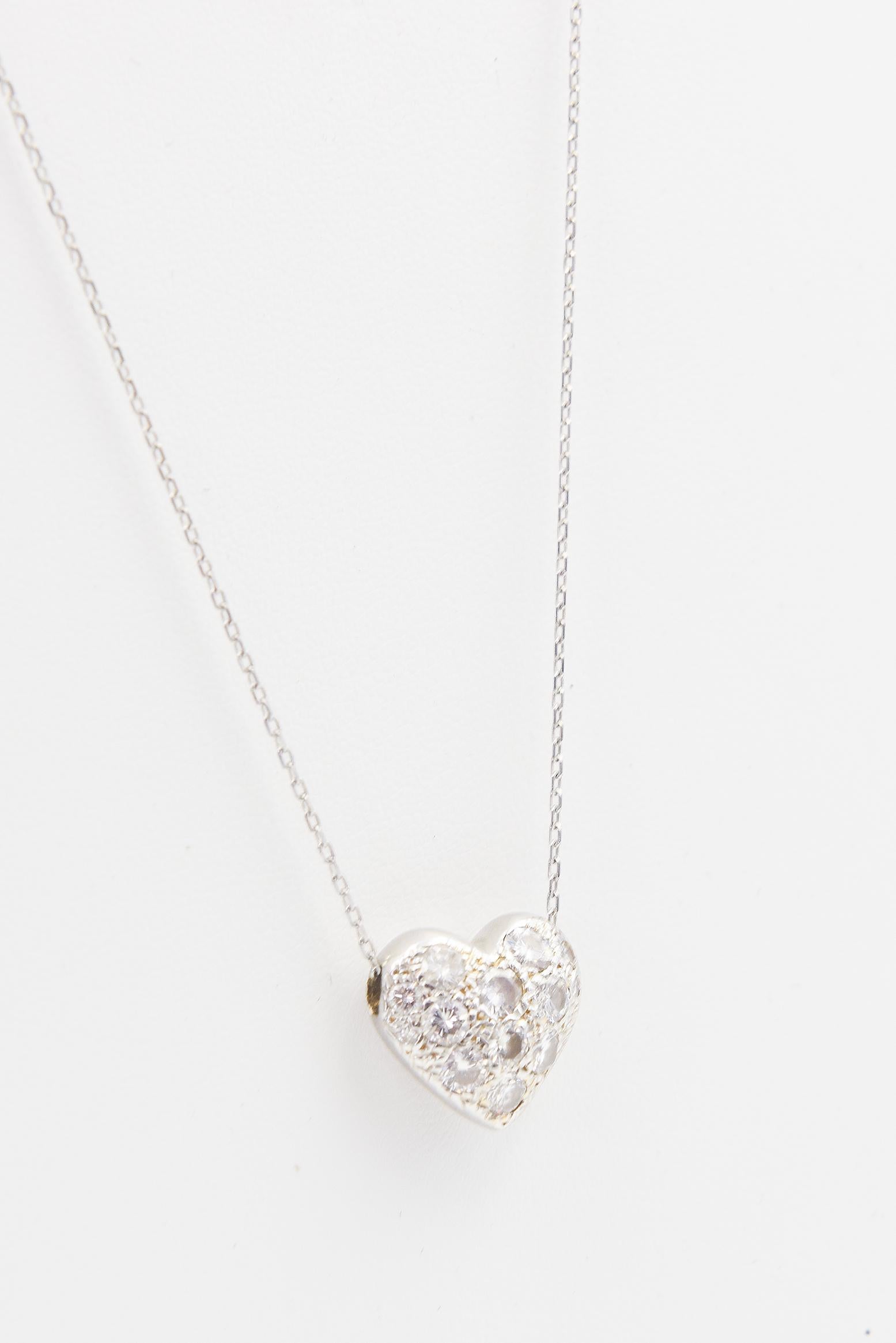 Pave diamond puffy heart 14k white gold pendant hanging on a sterling silver chain. The heart has 9 larger diamonds in the center and 4 smaller ones along the edges for a 1.10 carat approximate total weight in diamonds. The back side is a solid