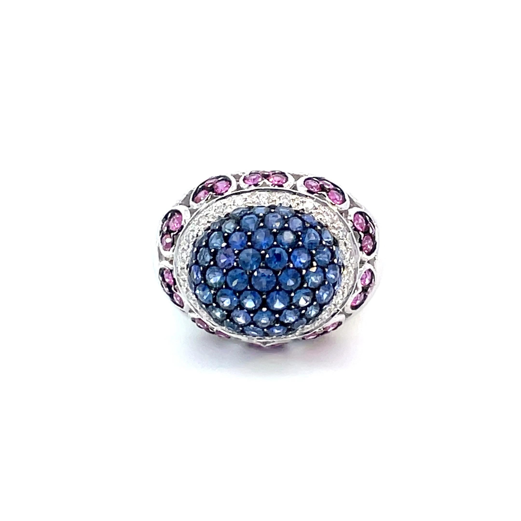 One dome ring set in centre with natural blue sapphires with a black rhodium finish surrounded by a row of brilliant cut white diamonds and below that a row of heart motif set with natural pink sapphires with a black rhodium finish in 18kt white