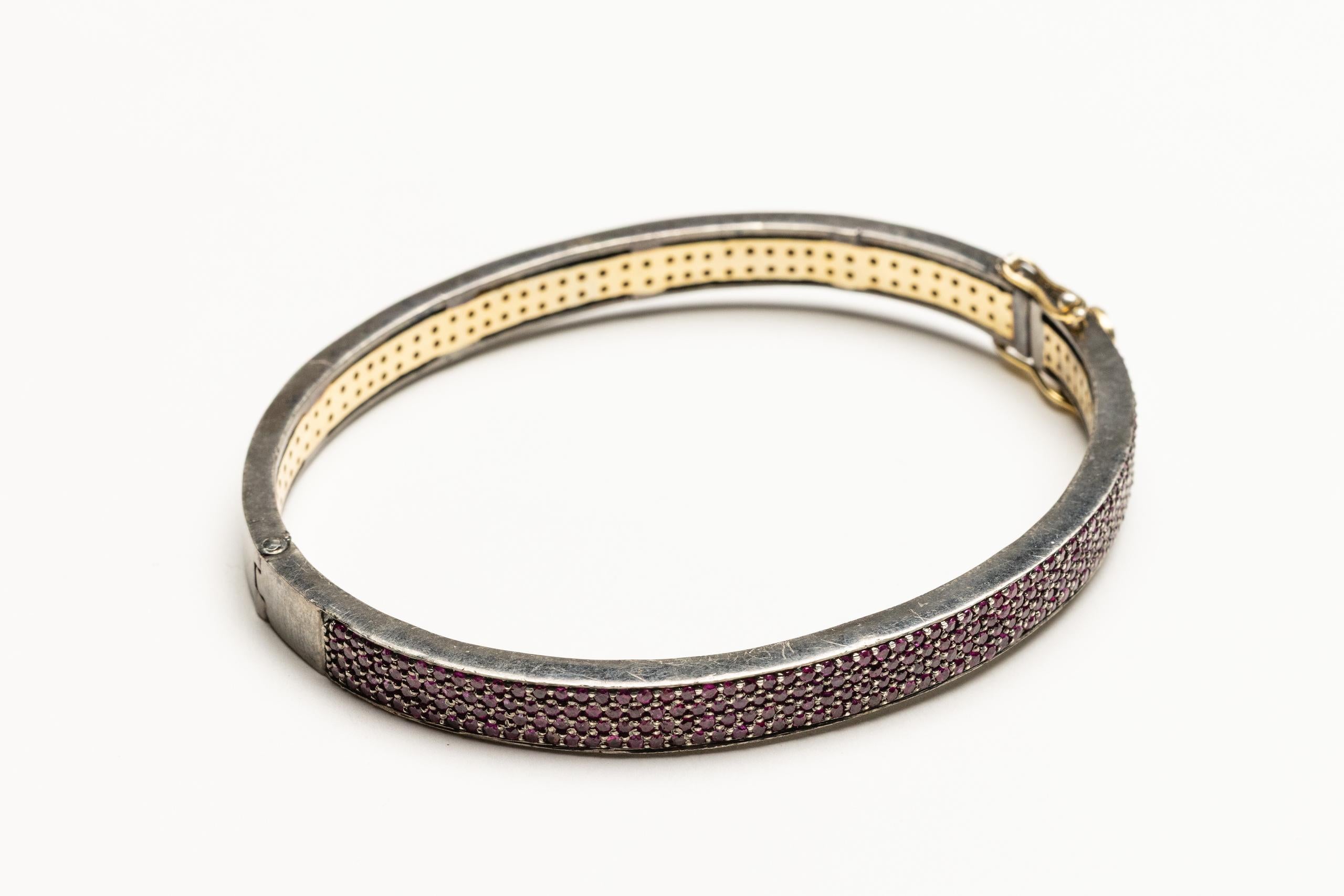 An oval bangle bracelet with clasp comprised of round, brilliant cut Burmese rubies in a pave` setting.  Set in an oxidized sterling silver.  Carat weight of rubies totals 3.21 carats.  Inside circumference is 7 inches.  The oval shape keeps the